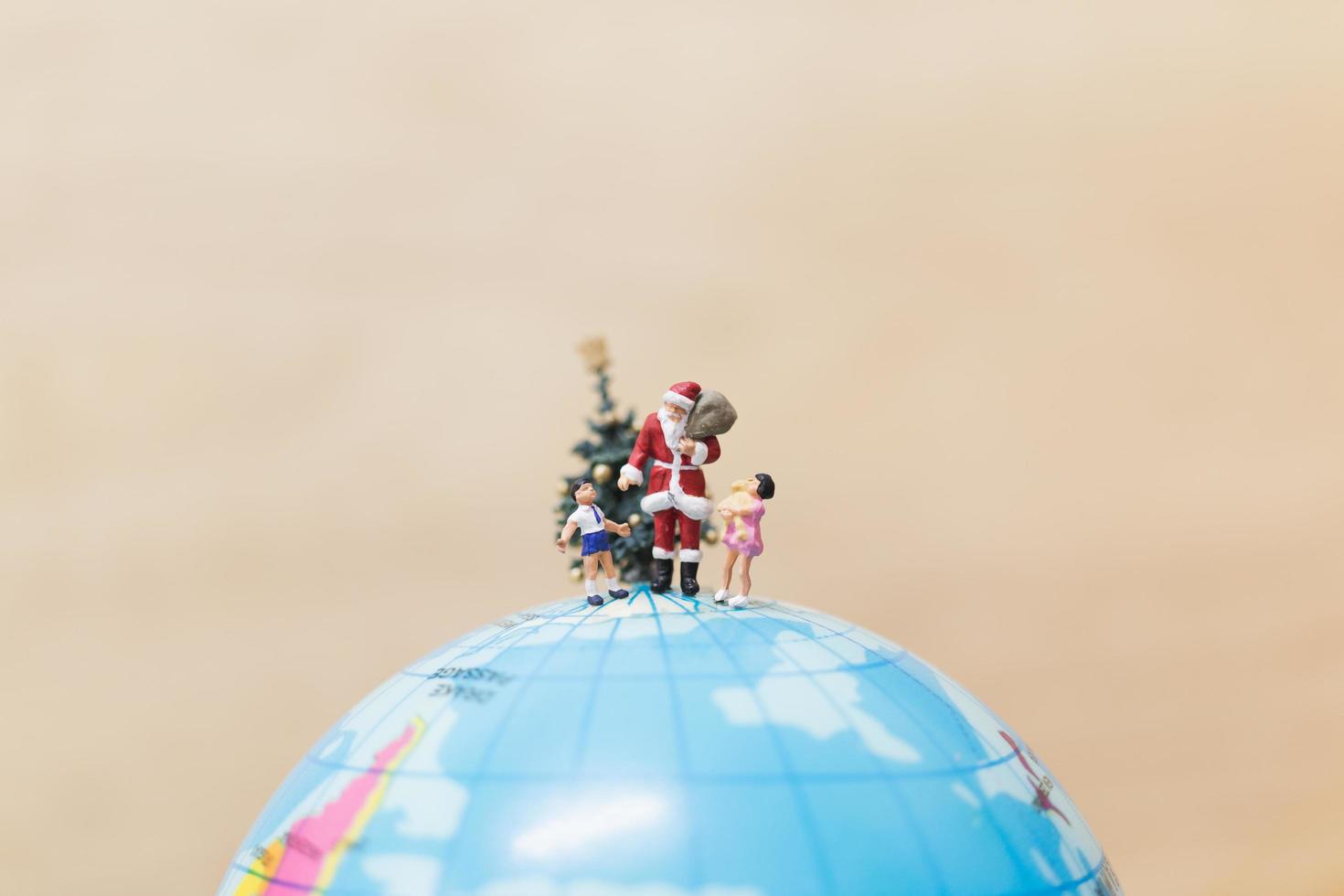 miniatyr jultomten håller gåvor för barn på en jordglob, god jul koncept foto