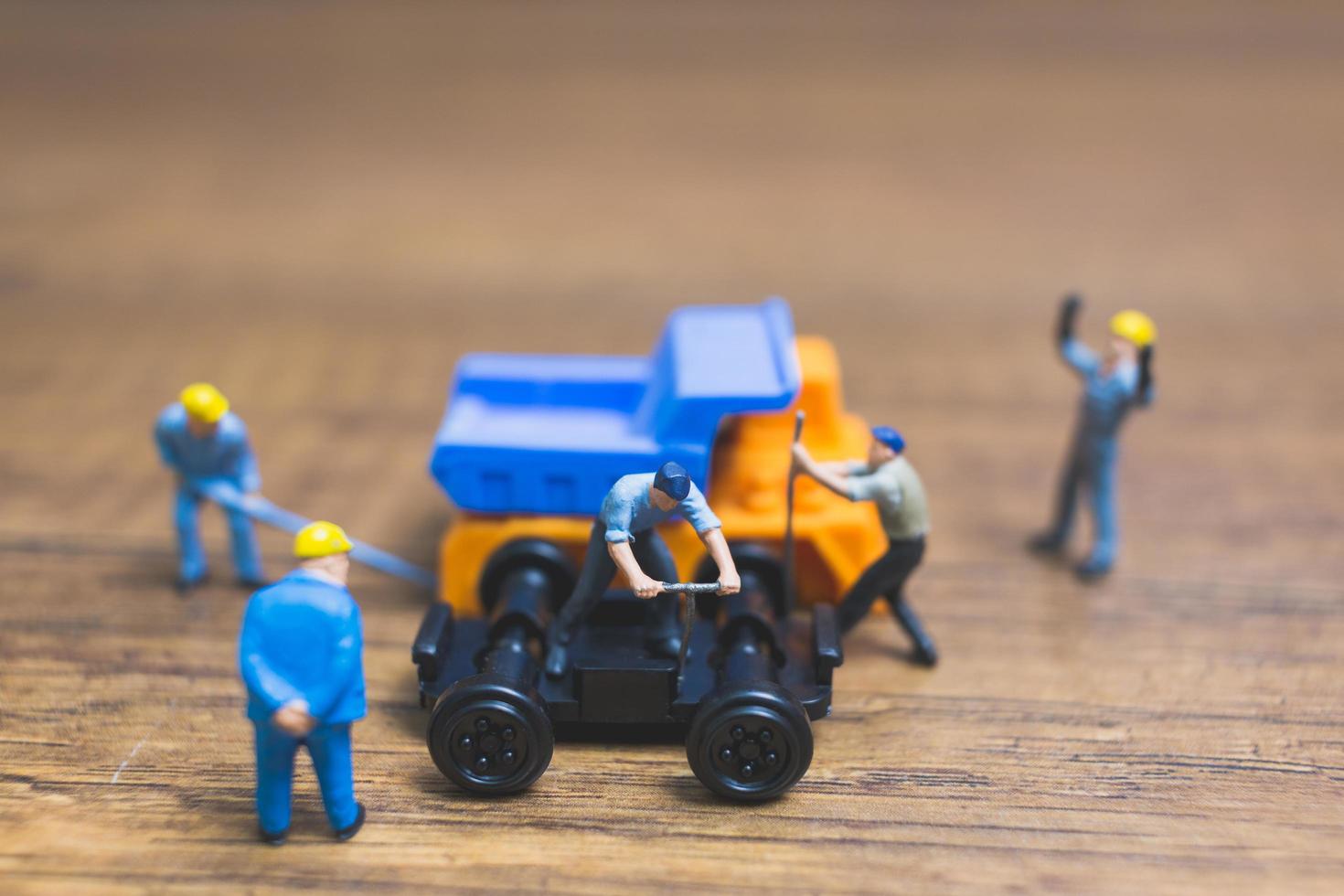 miniatyrarbetare som reparerar ett hjul från en lastbil på en träbakgrund foto