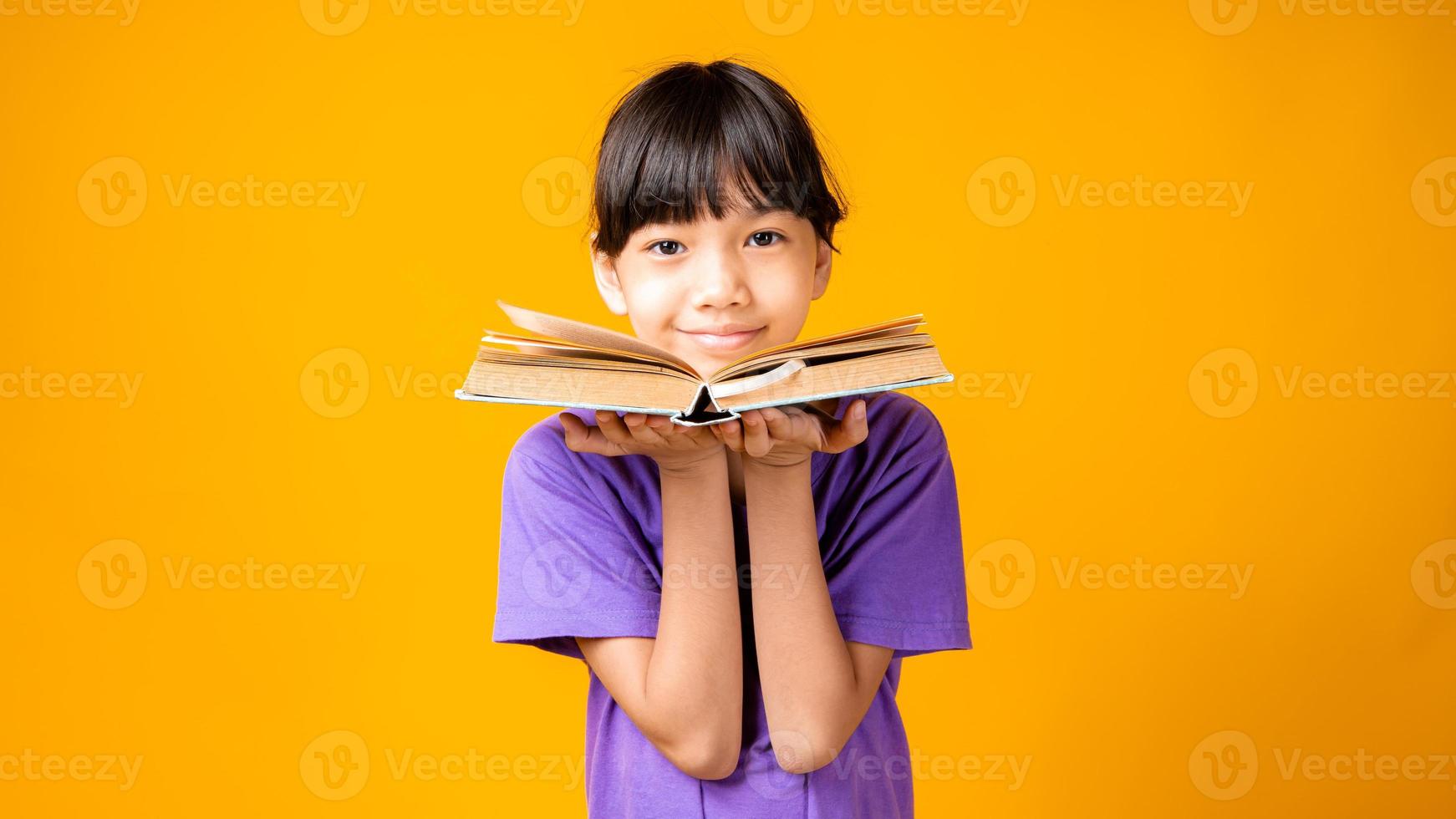 ung asiatisk tjej som ler i lila skjorta som håller den öppna boken i studio med gul bakgrund foto