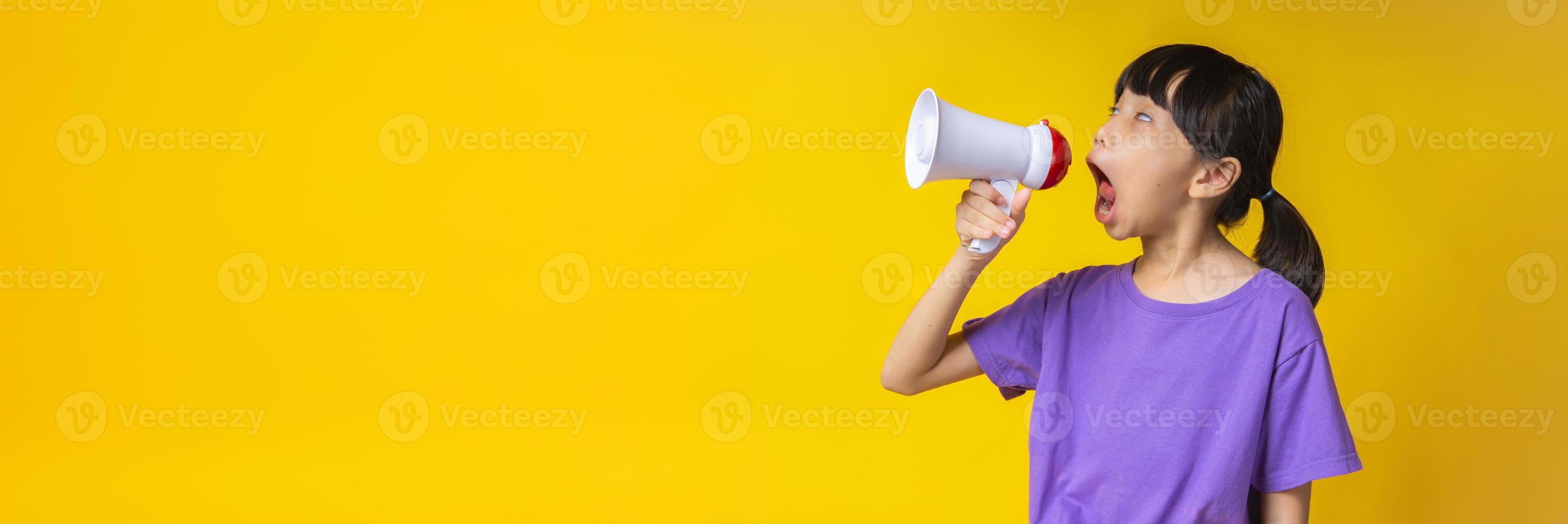 ung asiatisk tjej i lila skjorta som skriker in i vit megafon i studio med gul bakgrund foto