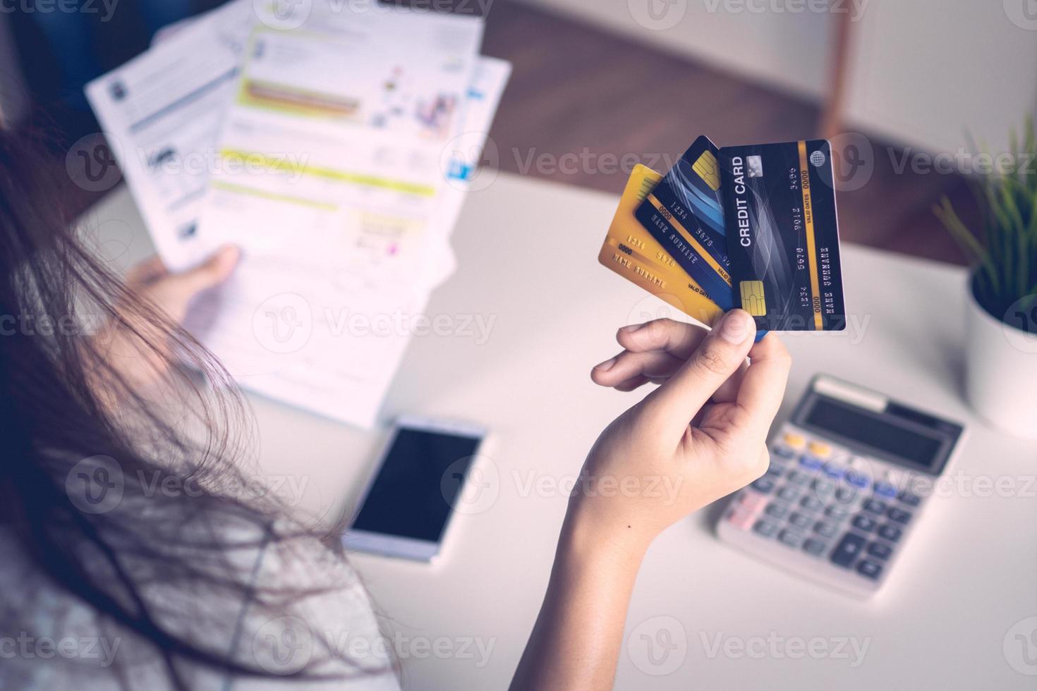 närbild kvinnans hand som håller tre kreditkort och papper vid ett skrivbord med miniräknare och en mobiltelefon foto
