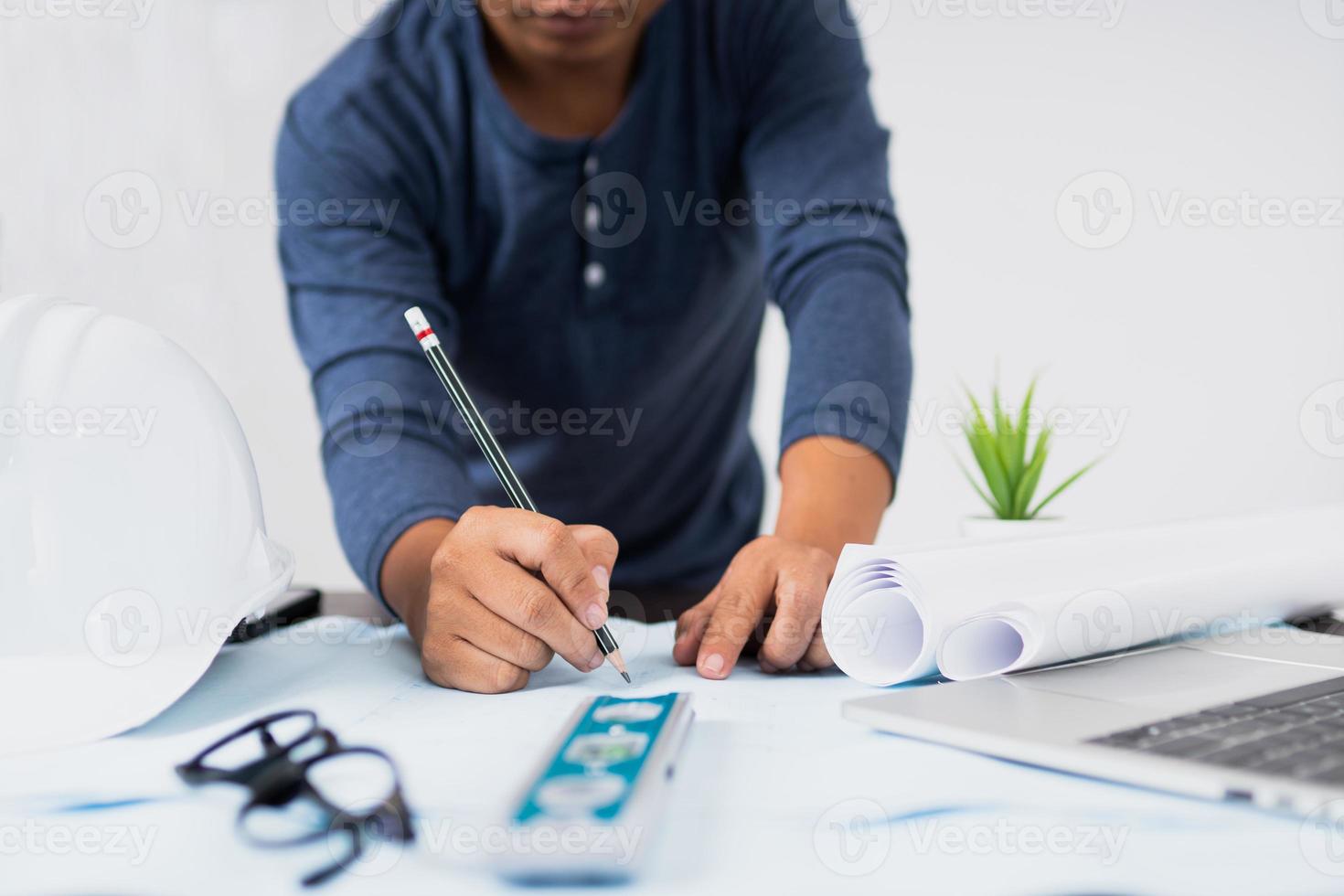person som arbetar på en ritning bredvid bärbar dator och rullat papper foto
