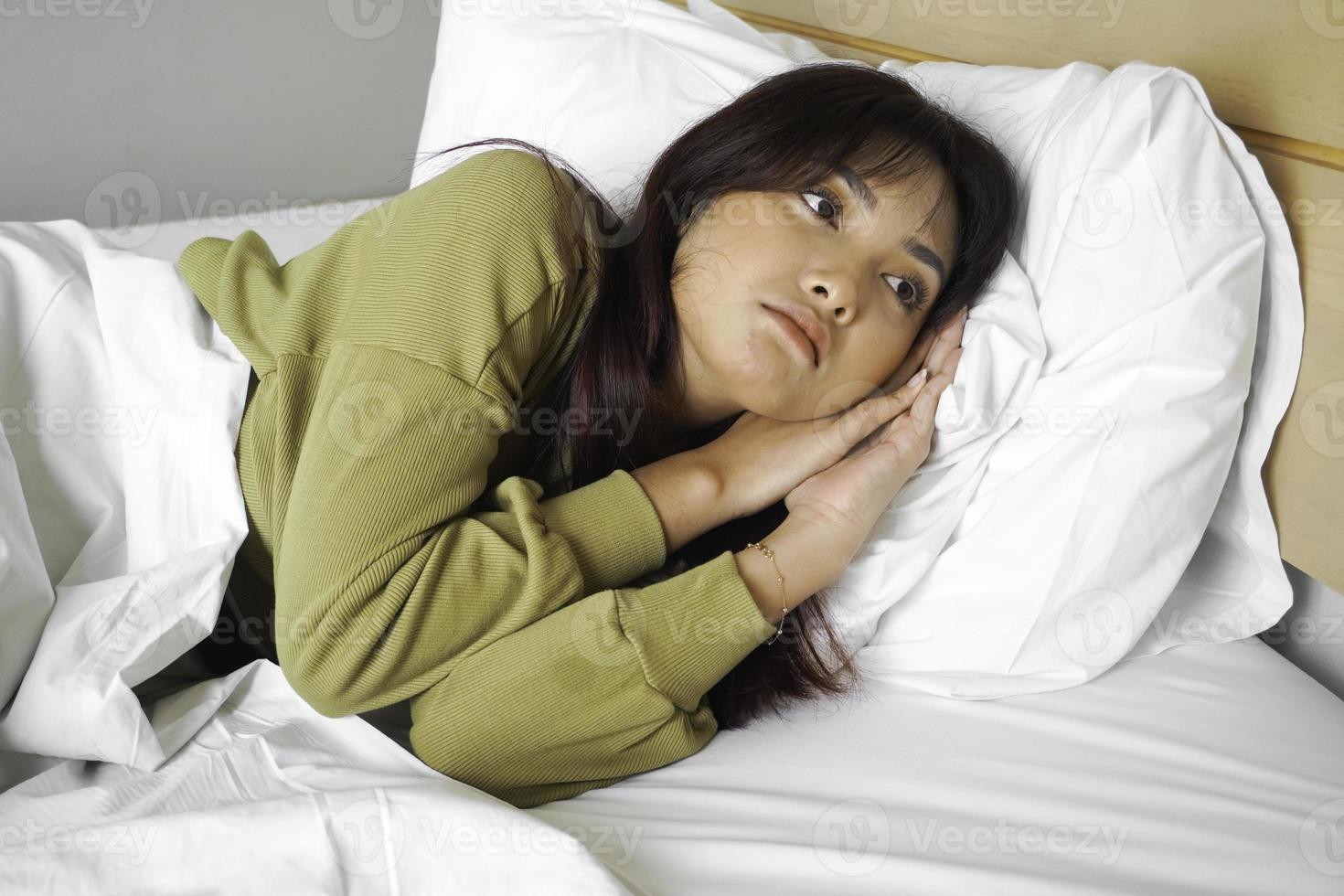 omtänksam asiatisk kvinna utseende eftertänksamt ovan klädd i tröja poser tänker handla om framtida medan liggande på de säng foto