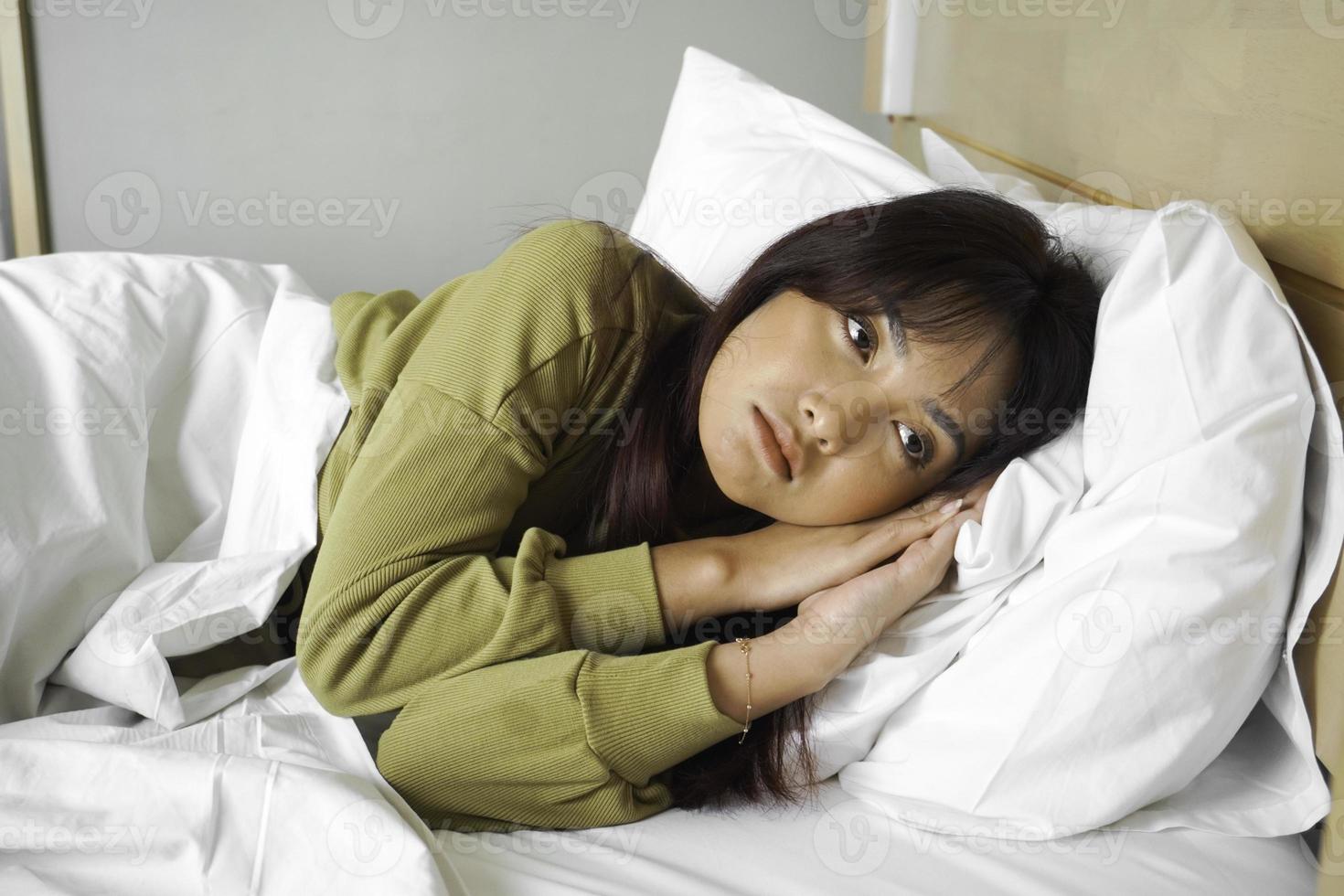 omtänksam asiatisk kvinna utseende eftertänksamt ovan klädd i tröja poser tänker handla om framtida medan liggande på de säng foto