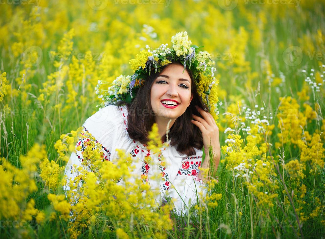 ung leende flicka i ukrainska kostym med en krans på hans huvud i en äng foto