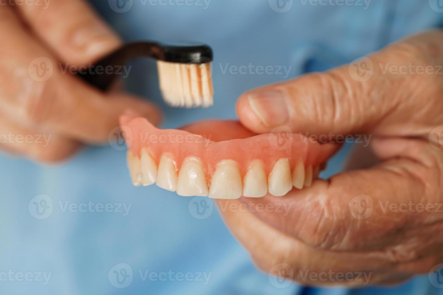asiatisk senior kvinna patient borsta tänder tandprotes med tandborste för Tugga mat. foto