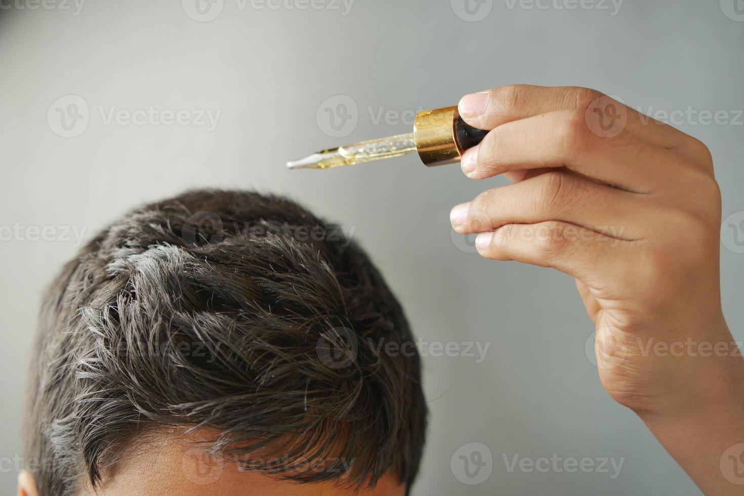 ung män applicering grundläggande oljor på hans hår foto