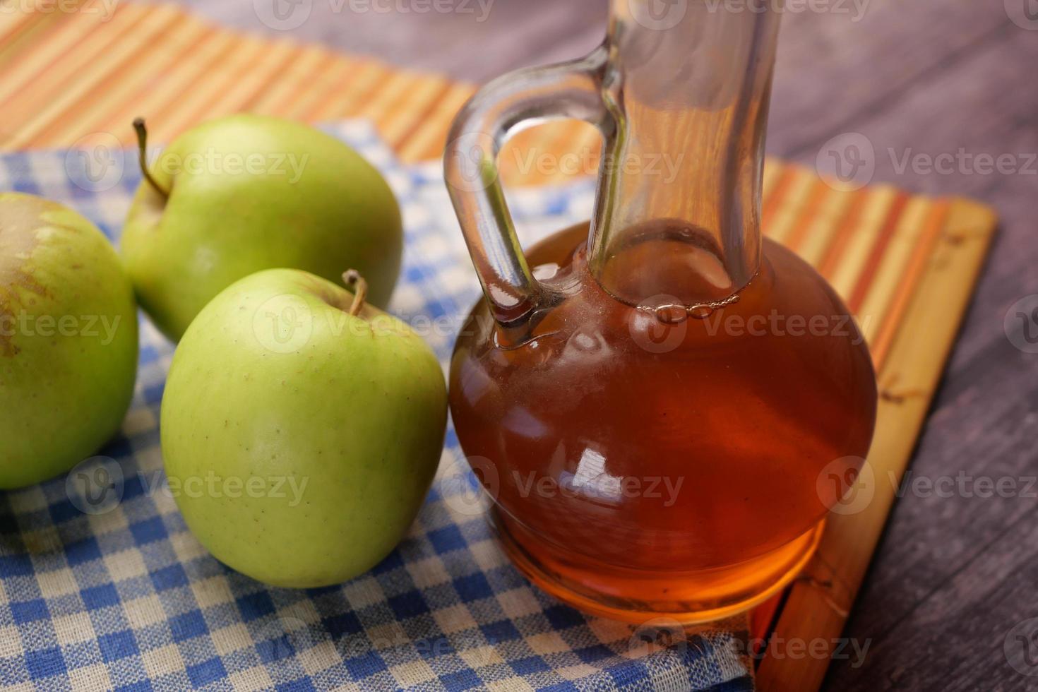 äppelvinäger i glasflaska med färskt grönt äpple på bordet foto