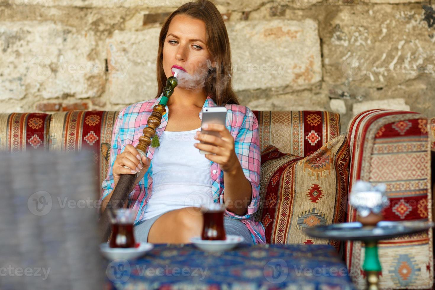 kvinna rökning en vattenpipa och användningar smartphone i en Kafé i istanbul, Kalkon foto