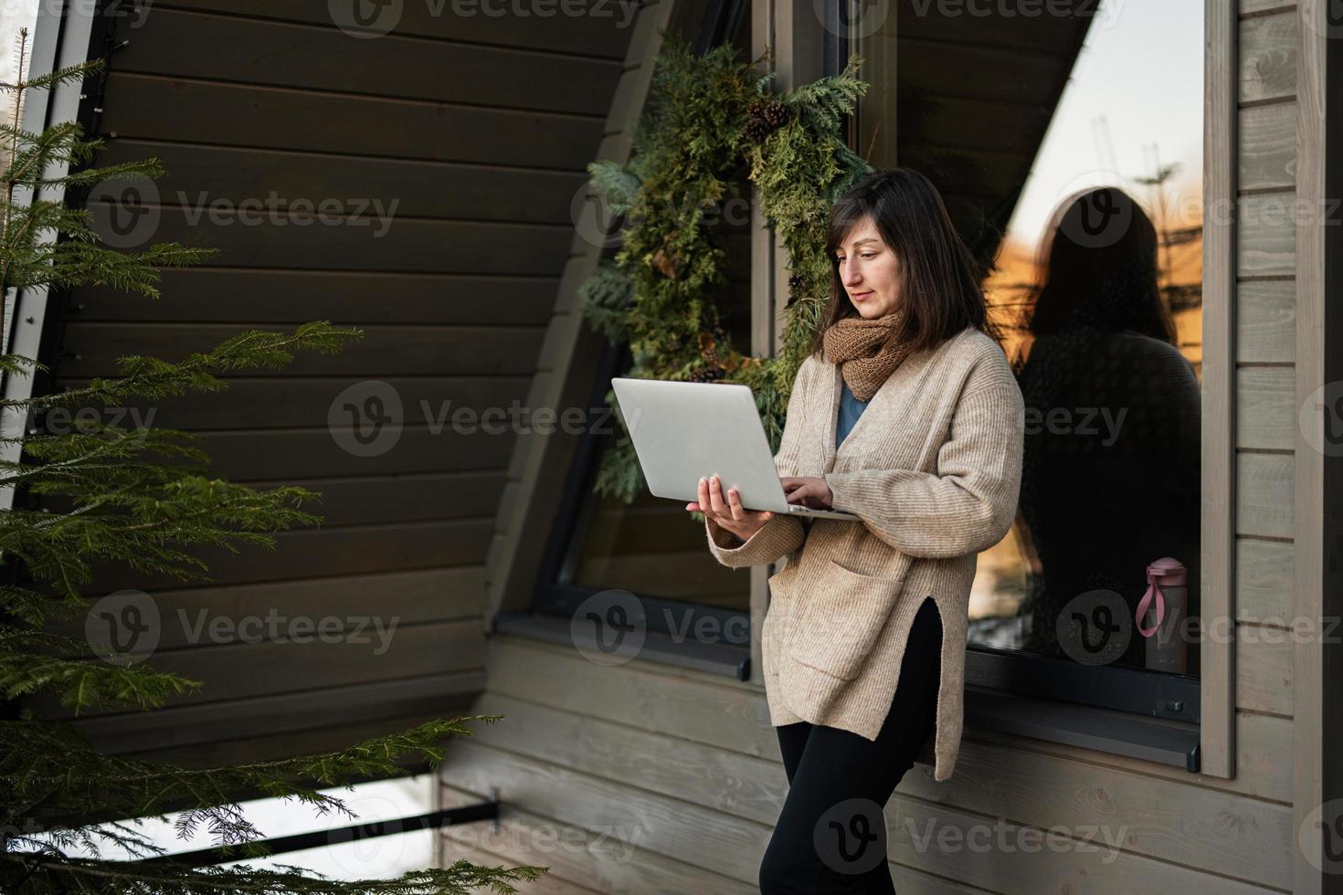 avlägsen arbete och flyr till natur begrepp. kvinna Arbetar på bärbar dator mot mycket liten stuga hus. foto