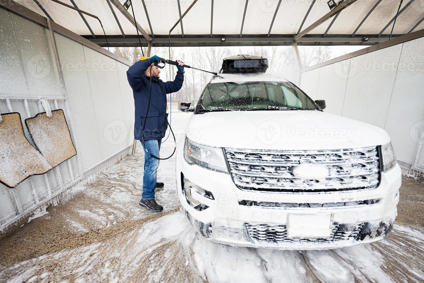 man tvättning hög tryck vatten amerikan sUV bil med tak kuggstång på själv service tvätta i kall väder. foto