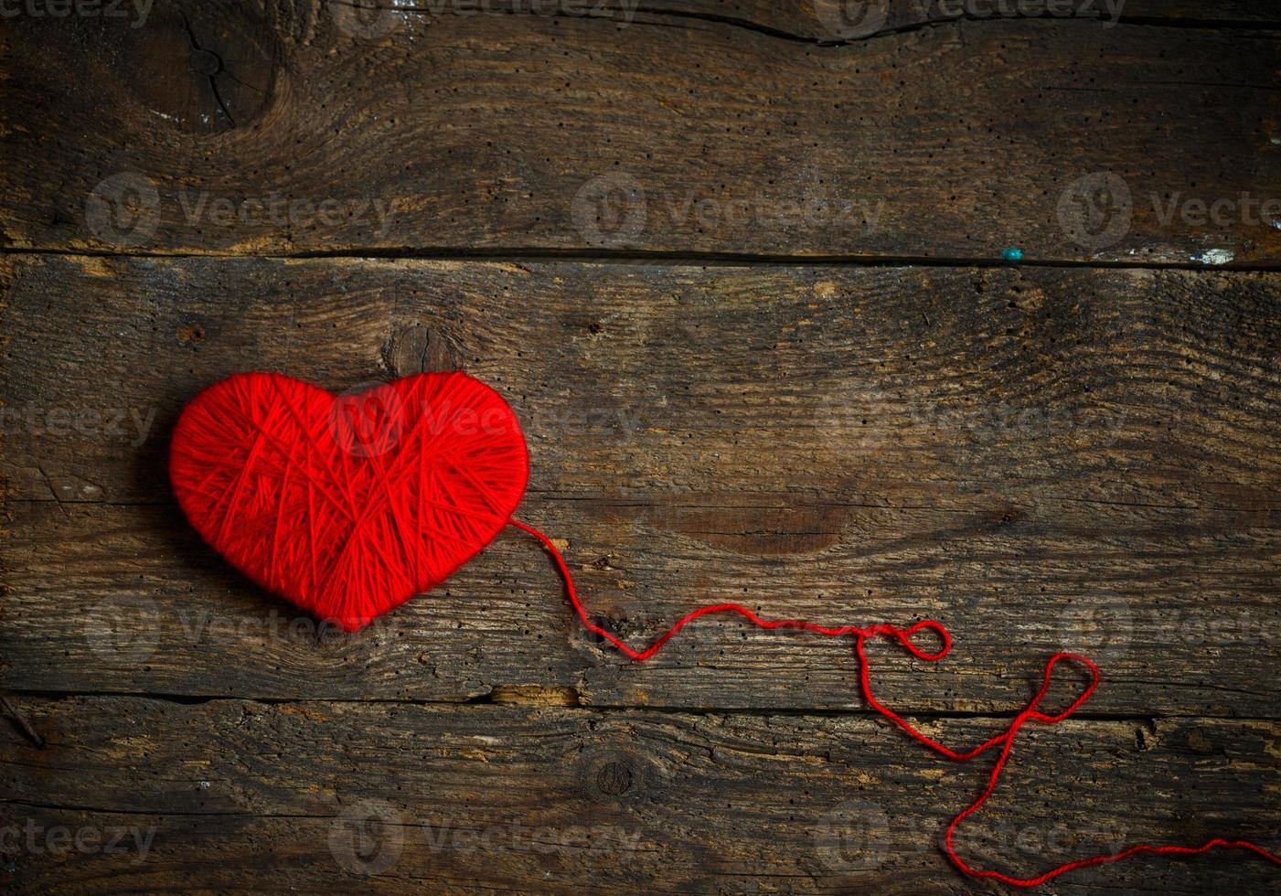 röd hjärta form tillverkad från ull på gammal sjaskig trä- bakgrund foto