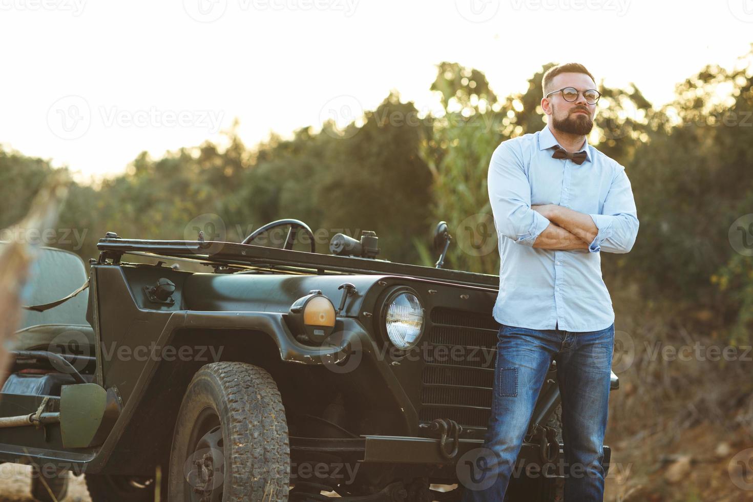 ung eleganta man med glasögon och rosett slips nära de gammaldags sUV foto