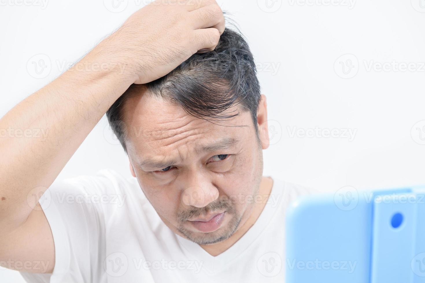en medelålders man lyser i de spegel och oroa handla om hår förlust eller hår grå foto