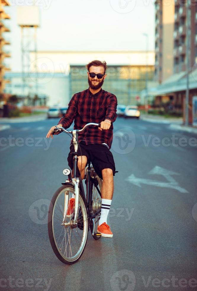 ung man i solglasögon ridning en cykel på stad gata foto