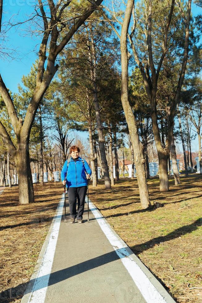 ett äldre aktiva kvinna promenader i de parkera på scandinavian pinnar. friska livsstil av vuxen kvinnor. foto