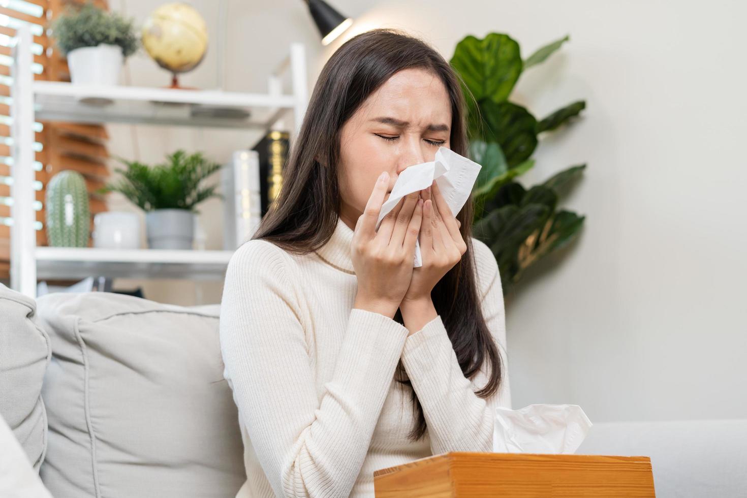 sjuk, coronavirus covid-19 asiatisk ung kvinna, flicka huvudvärk under filt ha en feber, influensa och använda sig av vävnader papper nysning näsa, rinnande Sammanträde på soffa säng på Hem. hälsa vård på virus person. foto