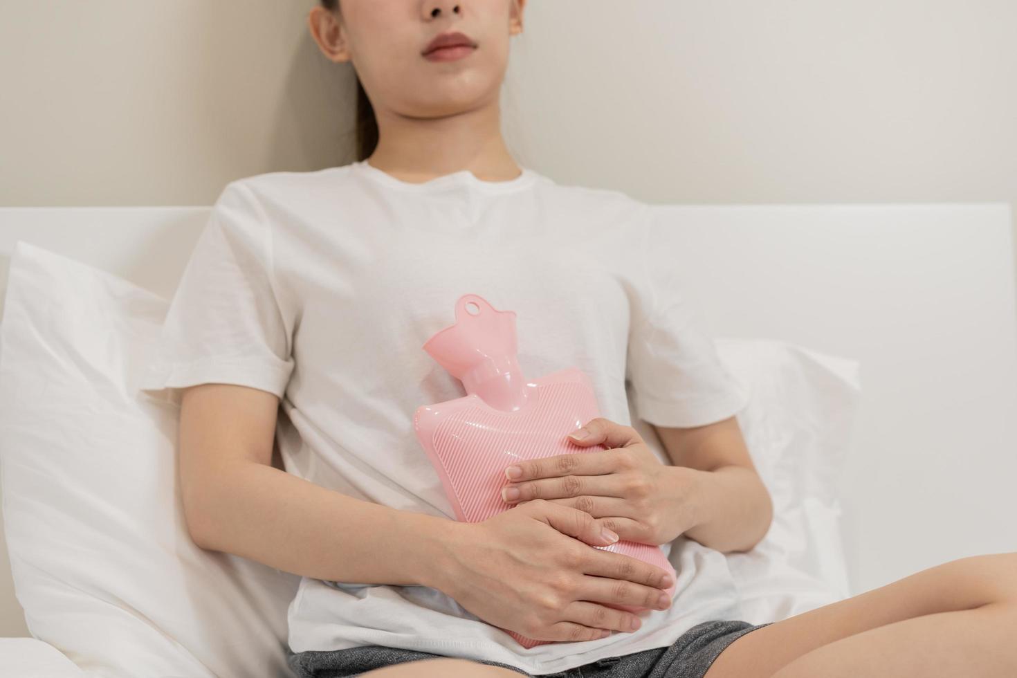 menstruation, period cykel av en gång i månaden, ont asiatisk ung kvinna, kvinna hand i magont, lida från premenstruell, mage eller buk smärta, använder sig av varm vatten flaska. hälsa problem inflammation i kropp. foto