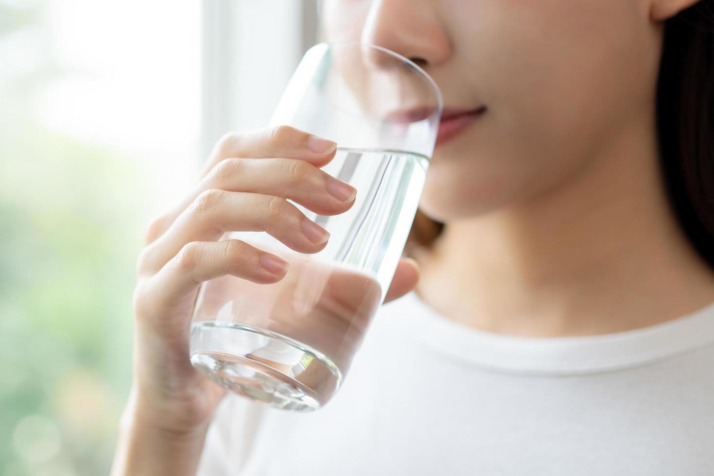 Lycklig skön, asiatisk ung kvinna, flicka dricka, smutta färsk glas av vatten för hydratisering av kropp, innehav transparent glas i henne hand, törstig på Hem. hälsa vård, friska livsstil begrepp. foto