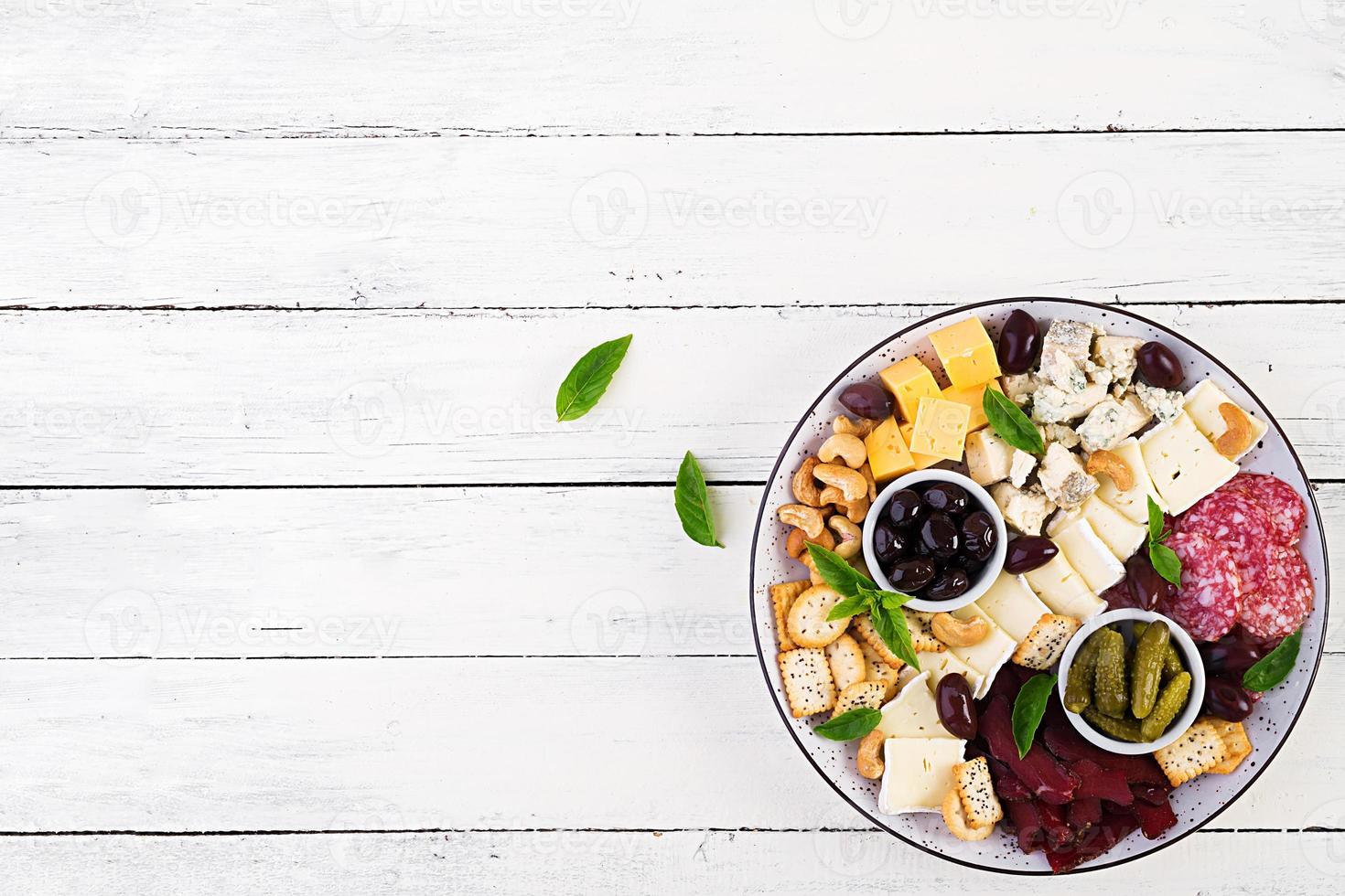 antipasto tallrik med basturma, salami, blå ost, nötter, ättiksgurka och oliver på en vit trä- bakgrund. topp se, över huvudet foto