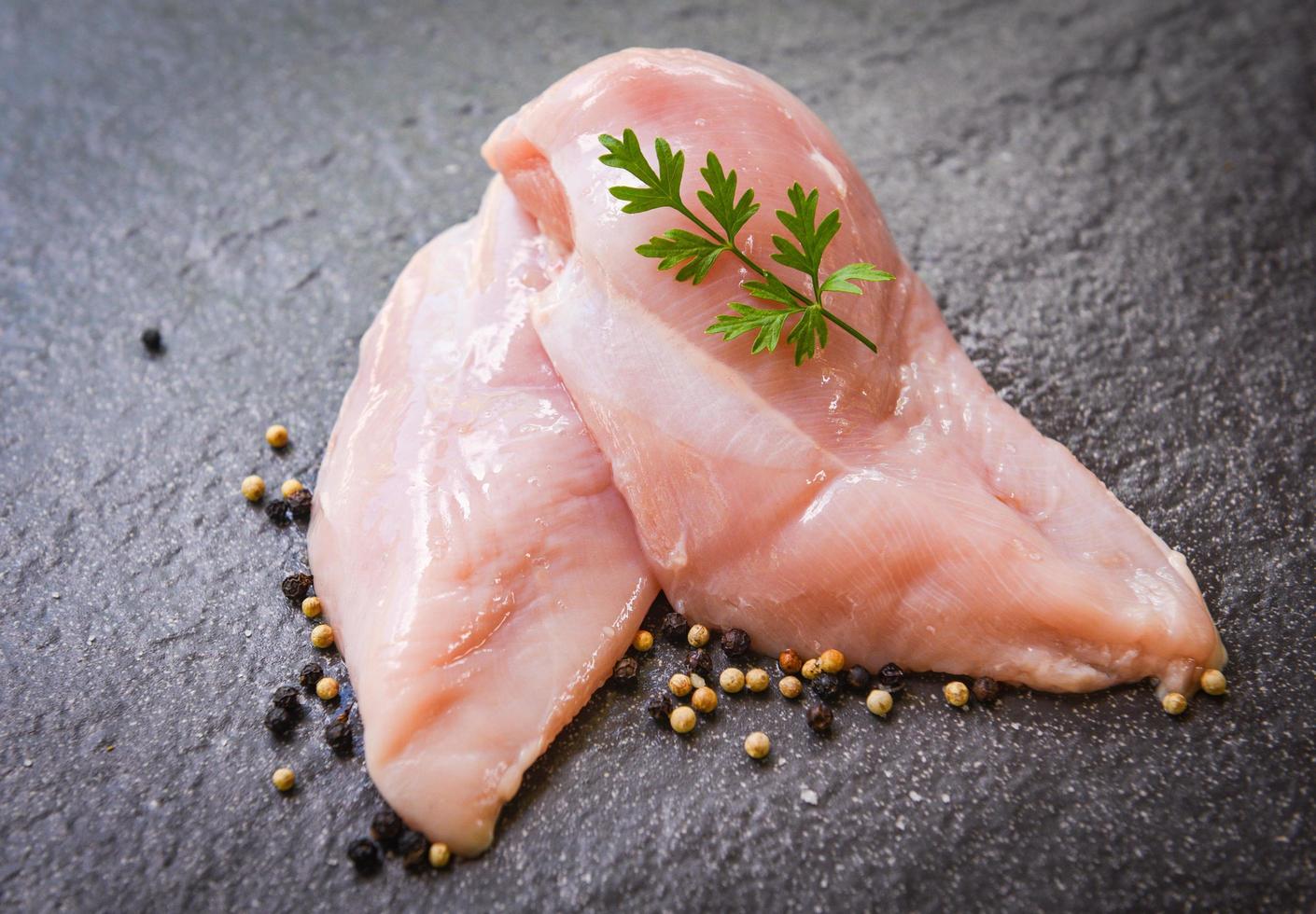 rå kyckling bröst med örter och kryddor på svart tallrik - rå okokt kyckling kött marinerad med Ingredienser för matlagning foto