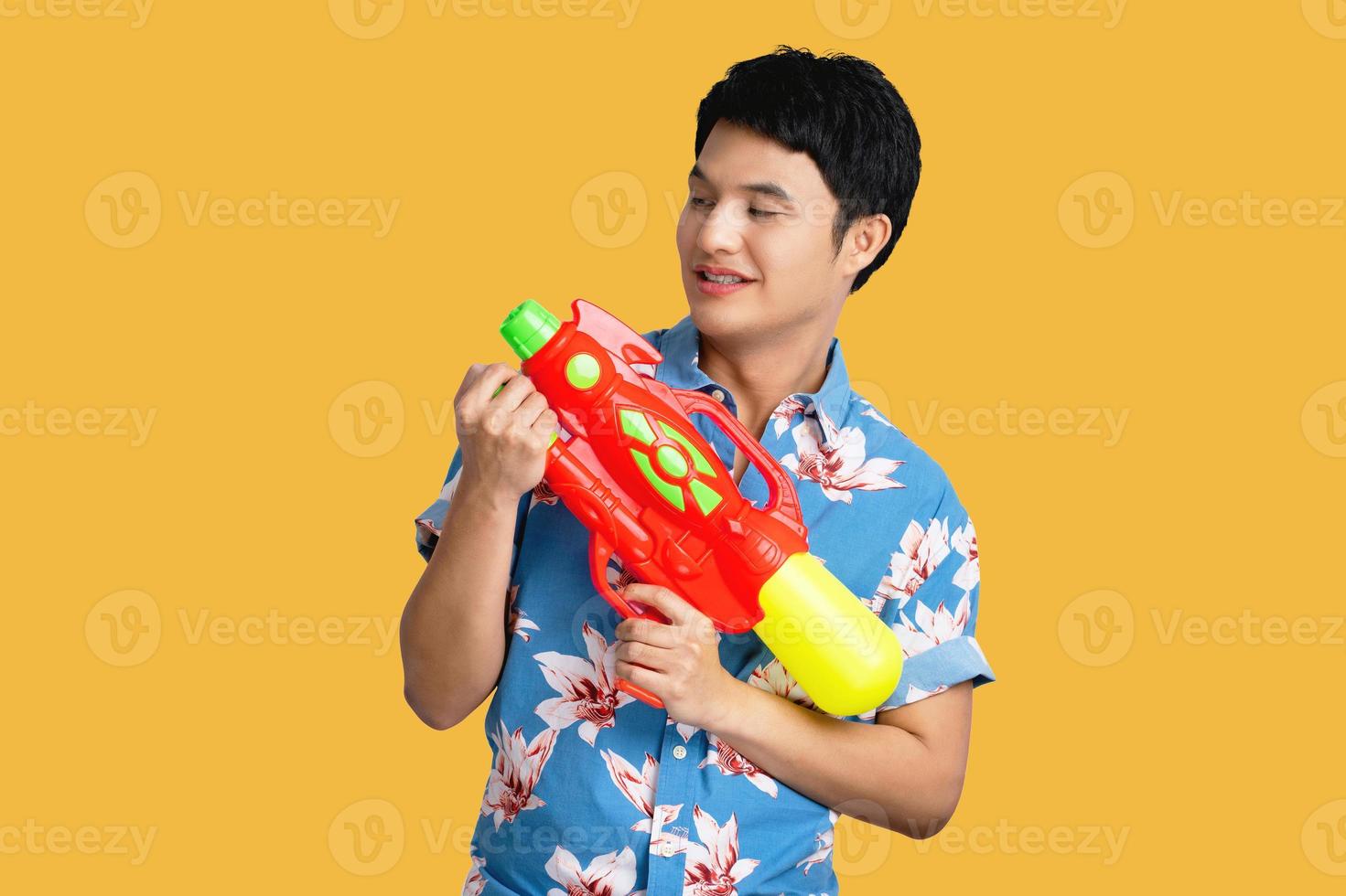 ung asiatisk man i de thai songkran festival. han innehar en vatten pistol och bär färger på en gul bakgrund. foto