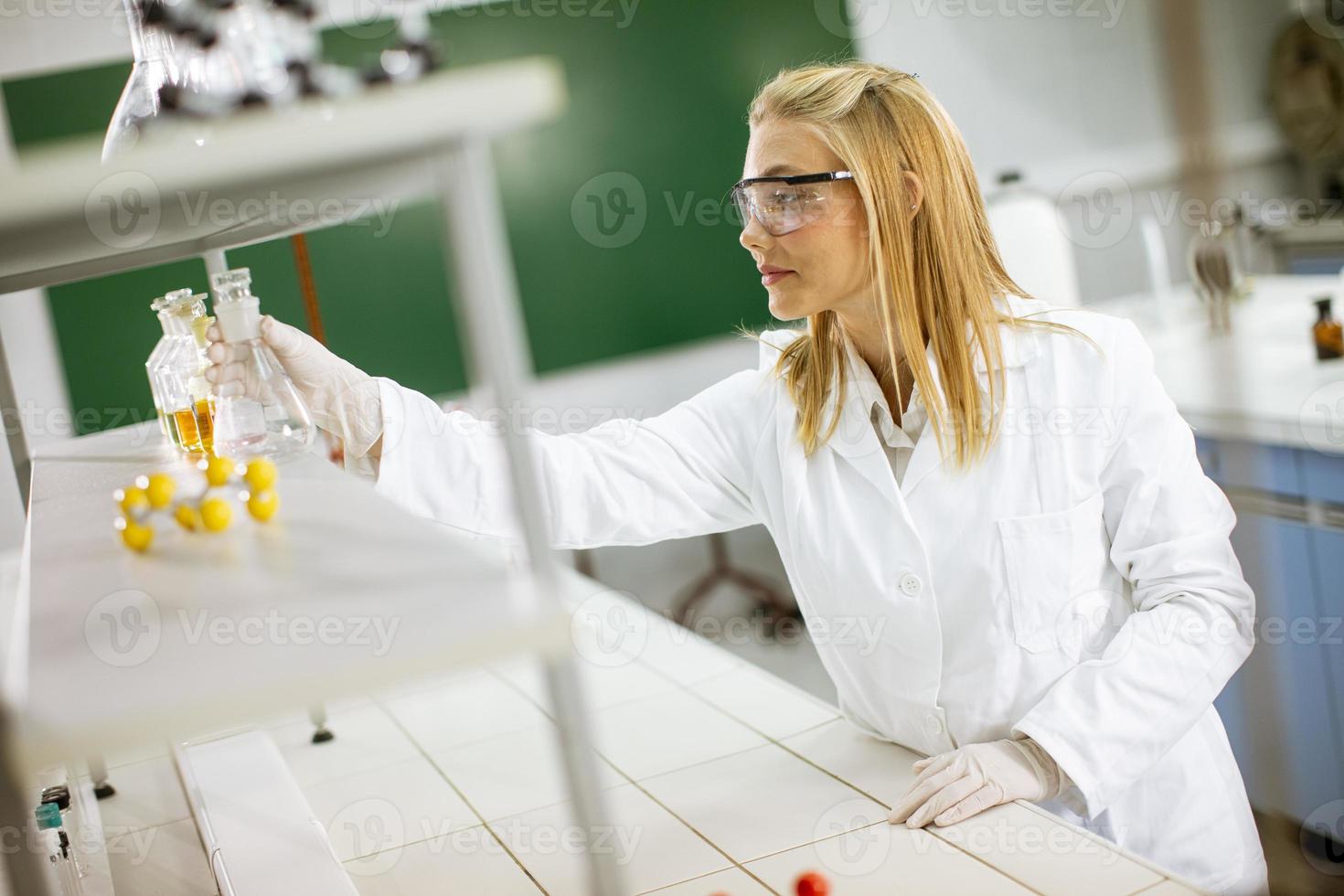 kvinnlig medicinsk eller vetenskaplig forskare som tittar på kolvar med lösningar i ett laboratorium foto