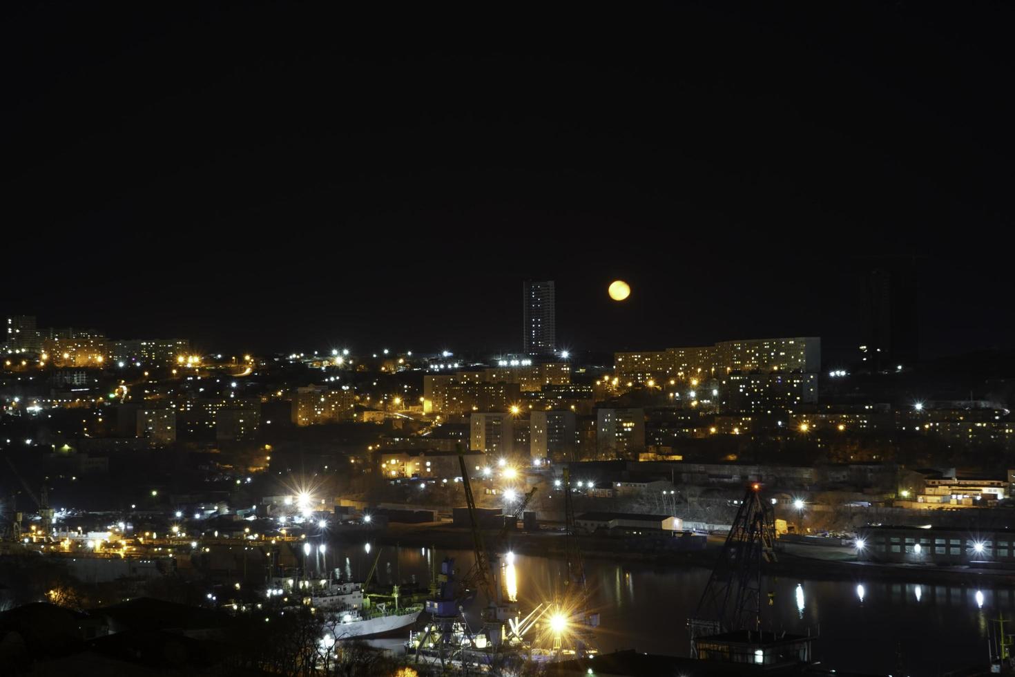 natt stadsbild med en kropp av vatten och gul måne i Vladivostok, Ryssland foto