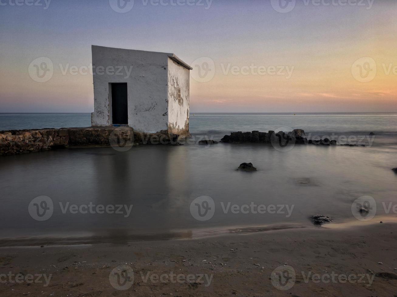 fiskarstuga vid solnedgången på några stenar nära stranden i Calpe, Alicante foto