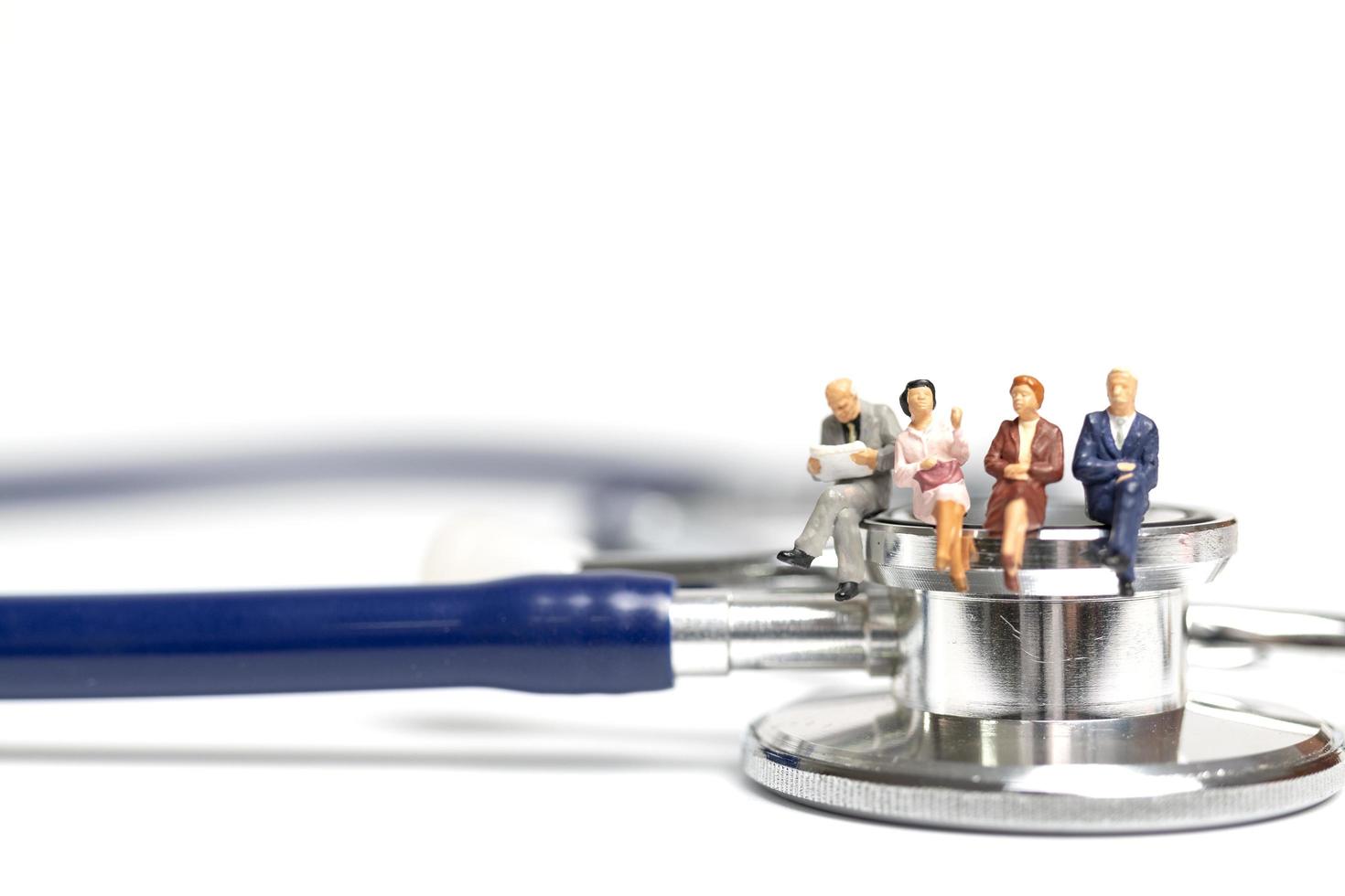 miniatyrfolk som sitter på ett stetoskop på en vit bakgrund, hälsovårdskoncept foto
