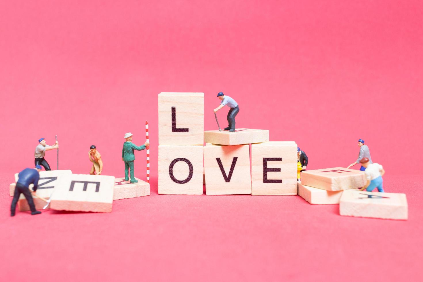miniatyrarbetare samarbetar för att bygga ordet kärlek på träklossar med rosa bakgrund, alla hjärtans dagskoncept foto