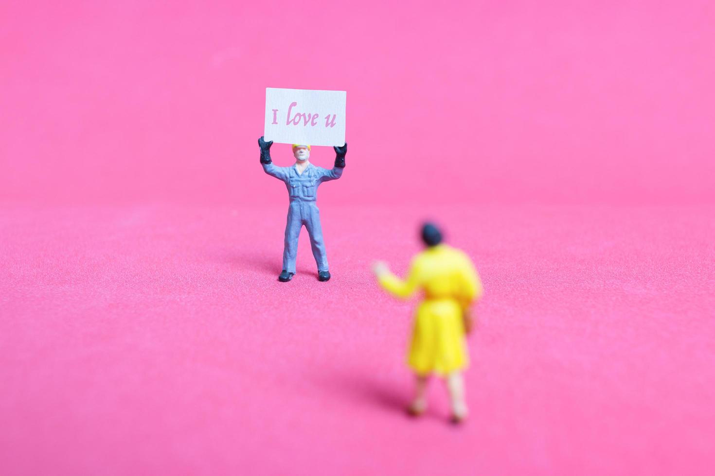 miniatyr person som håller en kartong med jag älskar dig på en rosa bakgrund, alla hjärtans dag koncept foto