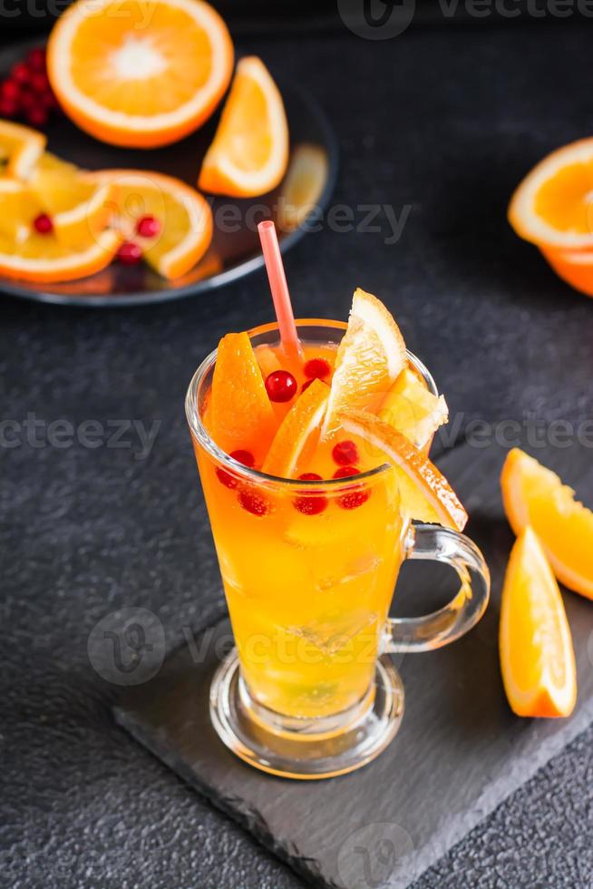 orange tranbär brusande cocktail i en glas och frukt och bär närliggande på en skiffer på en mörk bakgrund. hemlagad mocktail. vertikal se foto