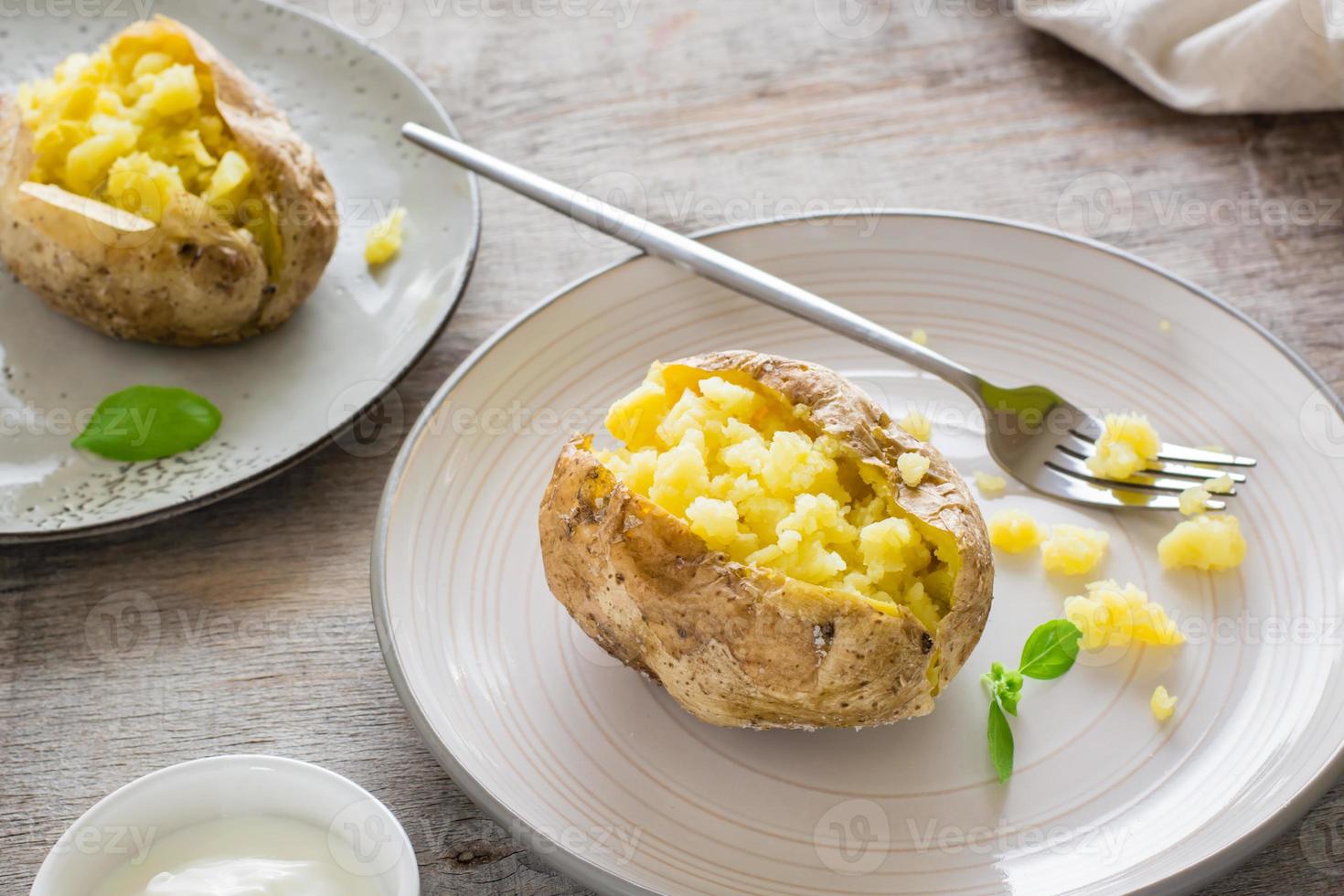 bakad potatisar i deras skinn på plattor och en skål av sur grädde på en trä- tabell. vegetarian naturlig mat. närbild foto