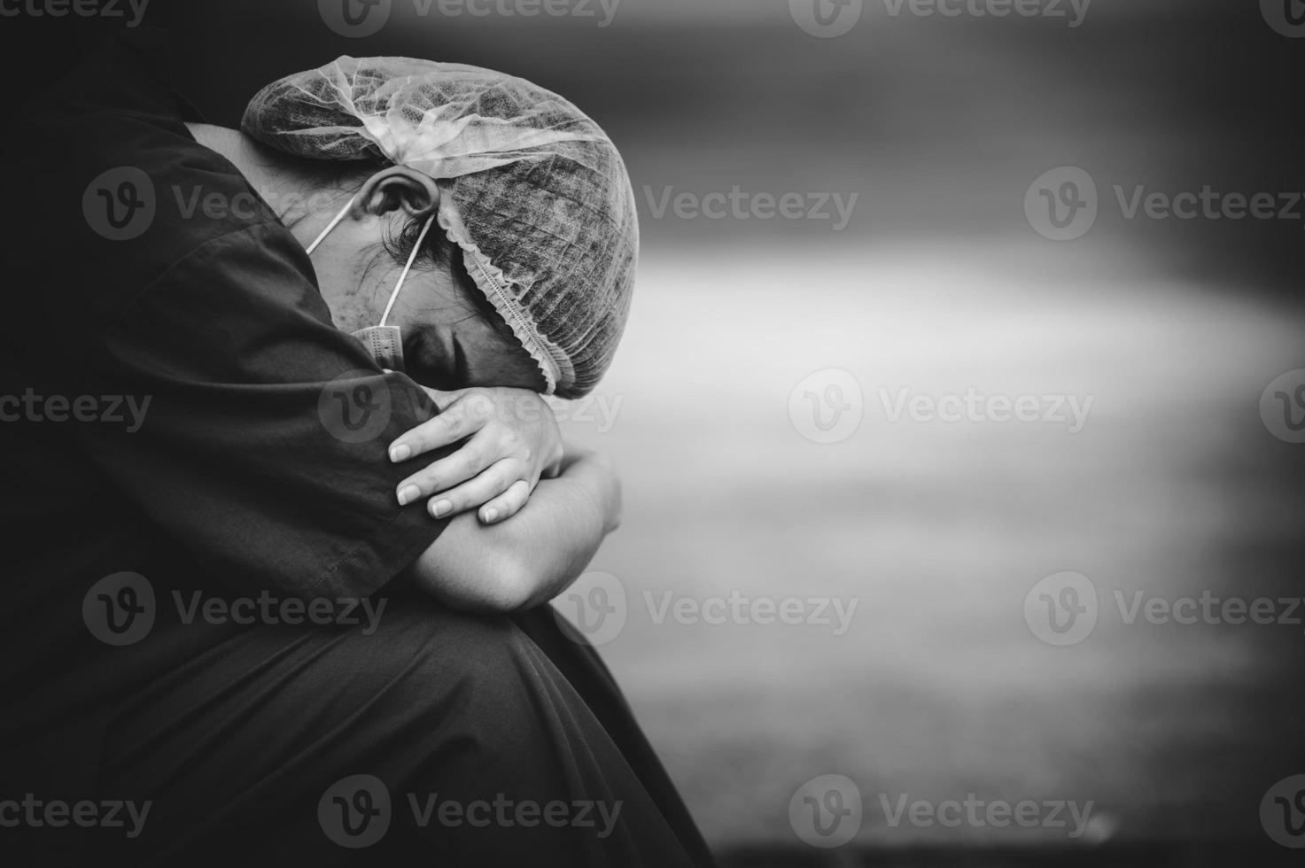 trött deprimerad kvinnlig asiatisk skrubbsköterska bär ansiktsmask blå uniform sitter på sjukhusgolvet, ung kvinna läkare stressad av hårt arbete foto