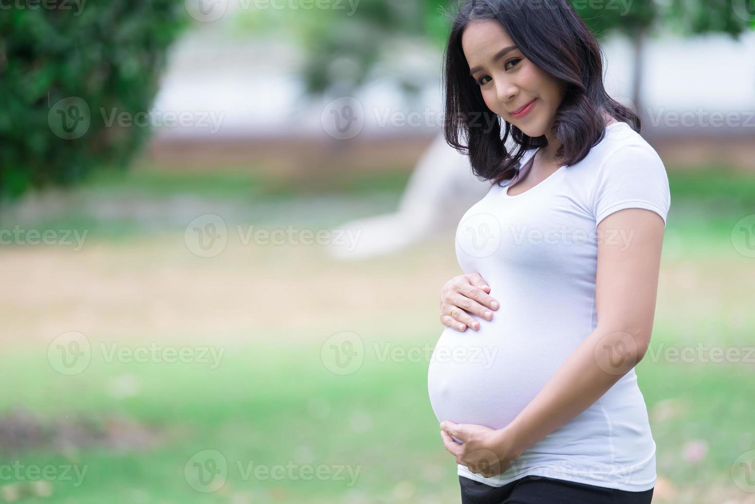porträtt av asiatisk skön gravid kvinna på de park, thailand människor, glada kvinna koncept, henne använda sig av hand Rör henne mage, mamma dag begrepp foto