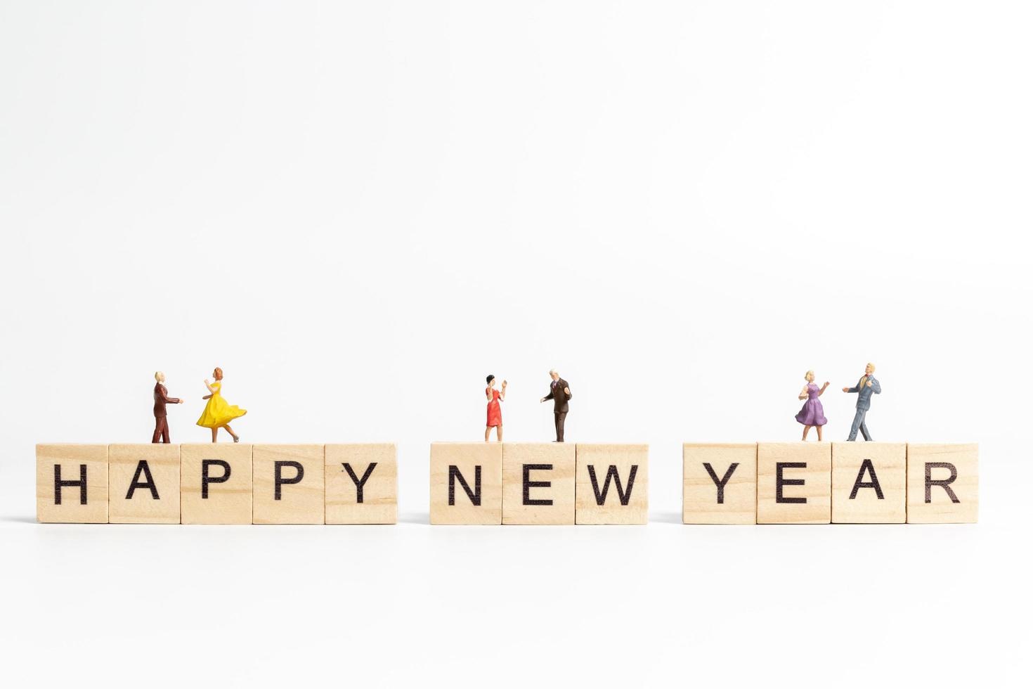 miniatyrfolk som dansar på träklossar med texten gott nytt år på en vit bakgrund foto