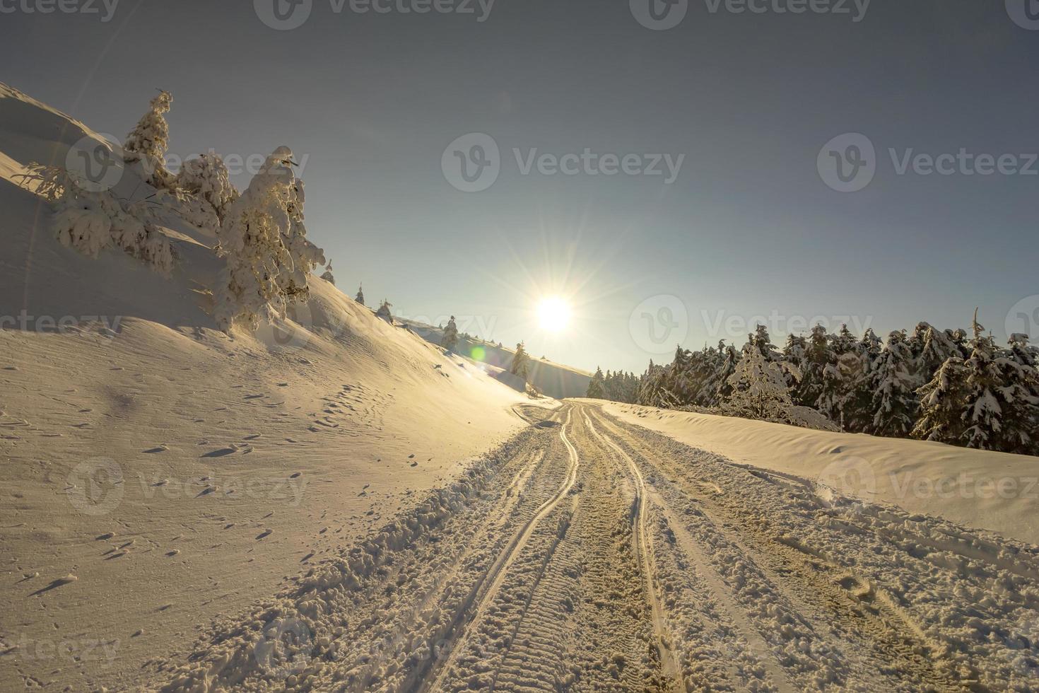 landskap med Sol, snö och bil spår på de väg i de vinter- i de berg. de begrepp av vinter- resa förbi bil. foto