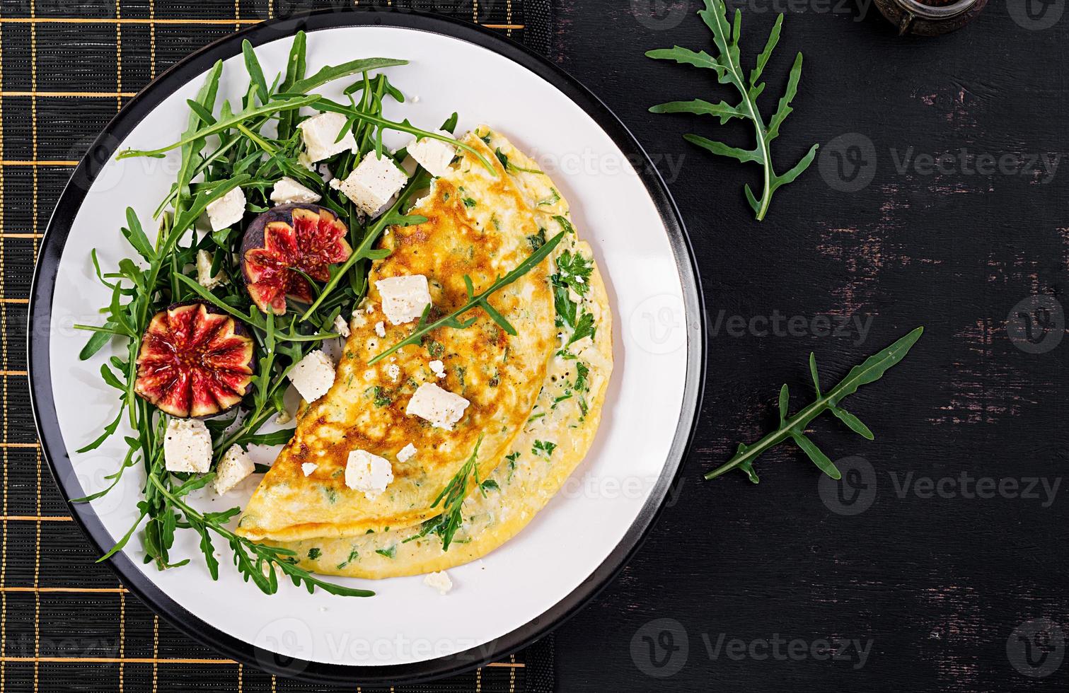 omelett med fetaost ost, persilja och sallad med fikon, arugula på vit tallrik. frittata - italiensk omelett. topp se. platt lägga. foto