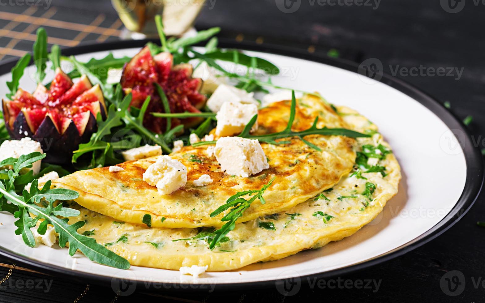 omelett med fetaost ost, persilja och sallad med fikon, arugula på vit tallrik. frittata - italiensk omelett. foto