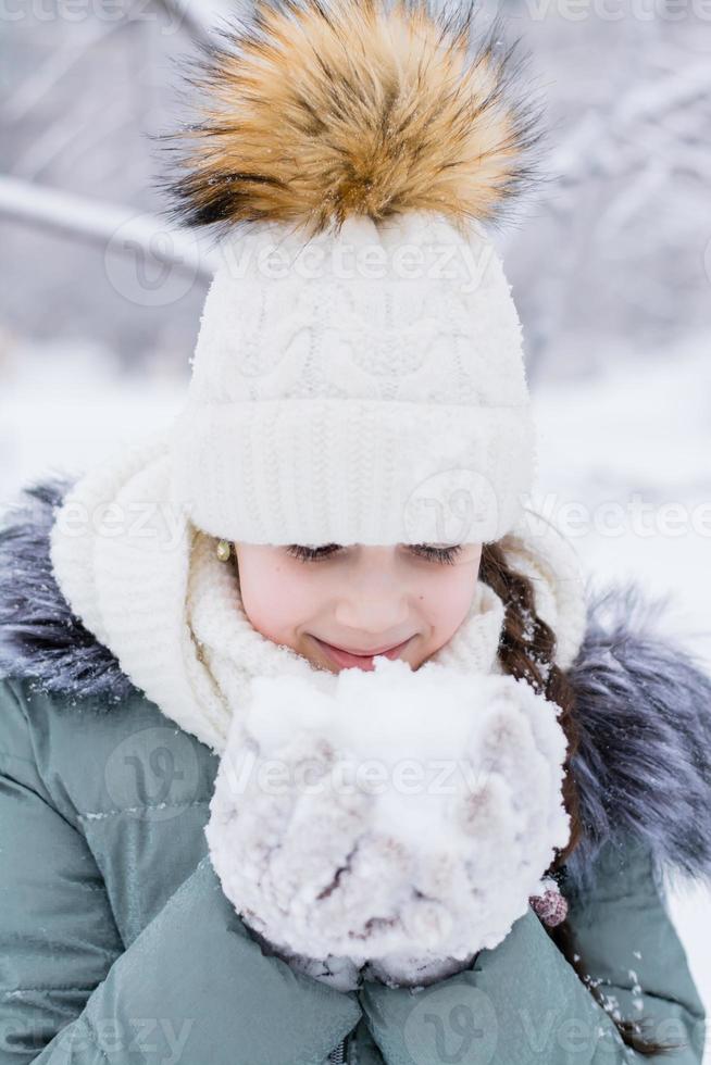 en flicka i värma kläder innehar snö i henne händer i handskar i en vinter- parkera. vinter- livsstil porträtt. vertikal se foto