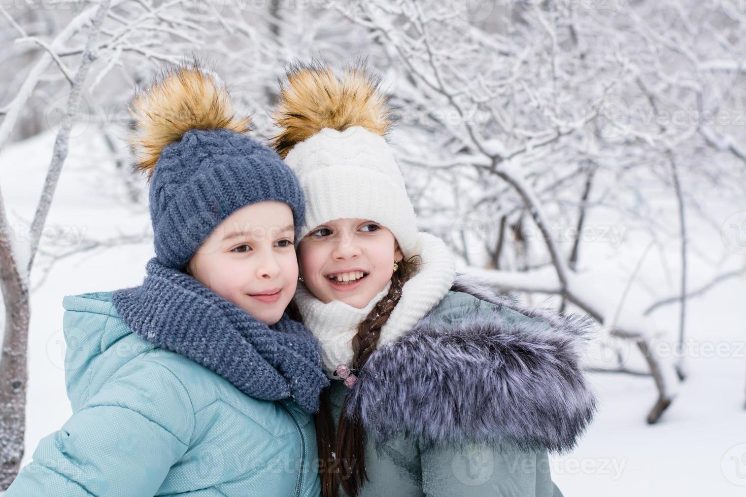 två leende flickor i värma kläder är kramas i en snöig parkera. vinter- promenader, livsstil foto