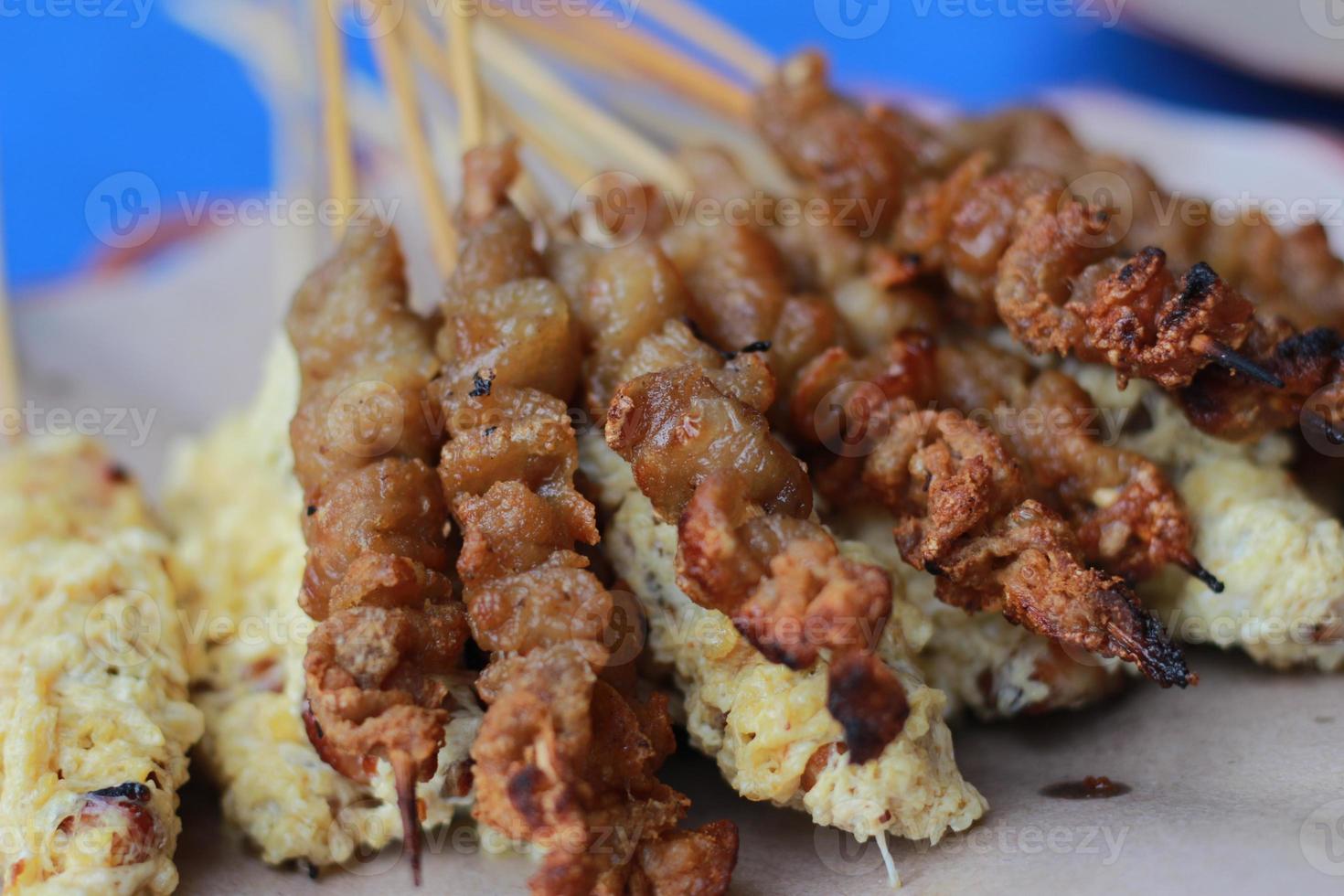 Foto av kyckling satay överdragen med friterad ägg och kyckling inälvor satay eras med röd chili sås. indonesiska mat kallad sate taichan. mat begrepp Foto.