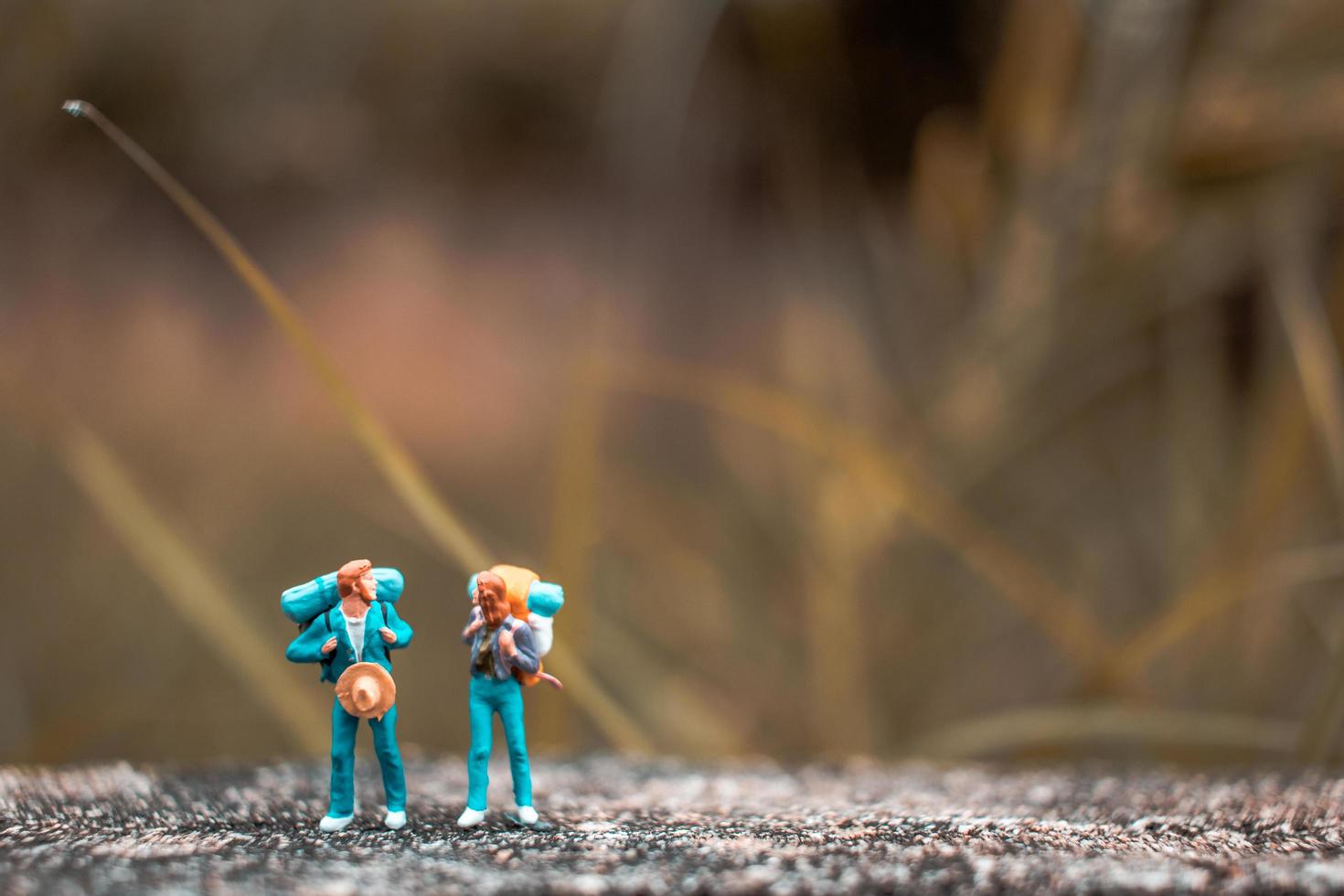 miniatyrbackpackers som står på ett betonggolv med en bokeh-naturbakgrund foto