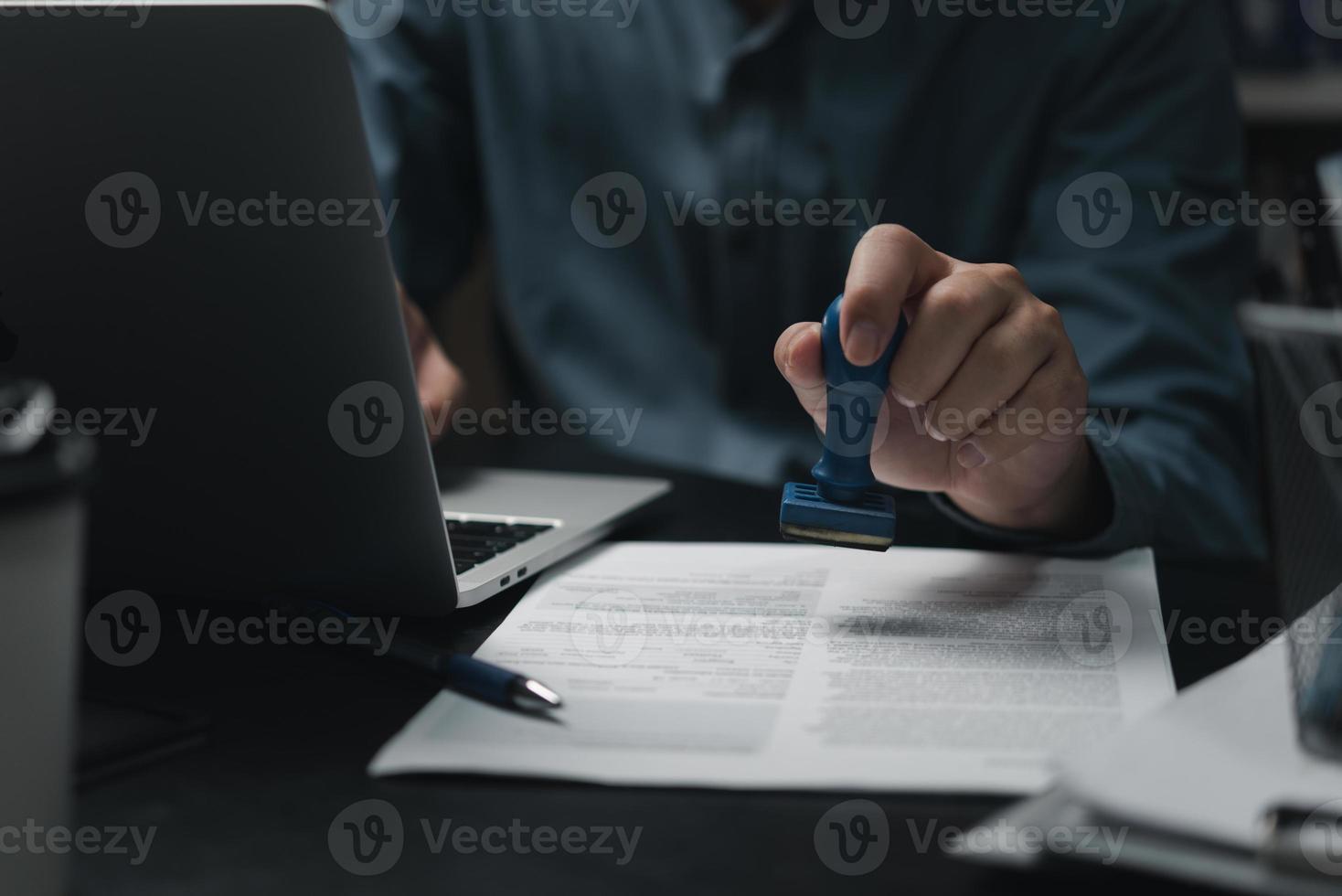 affärsman hand stämpling godkänd på certifikat dokumentera kontrakt i kontor. advokat stämpling tillåta på pappersarbete på trä- skrivbord. foto