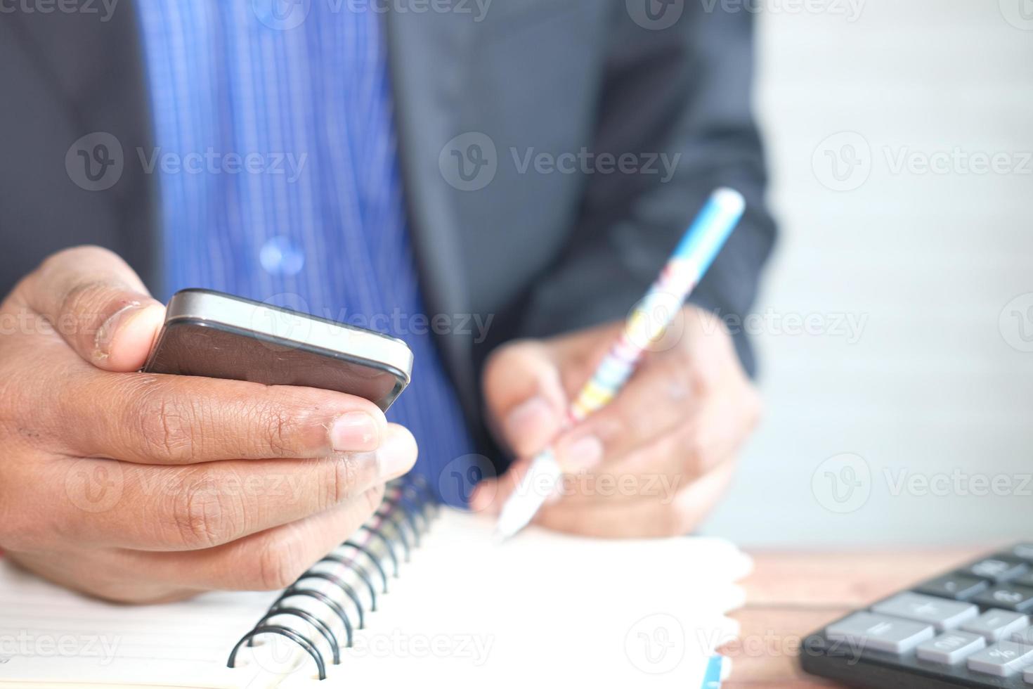 ung man som använder smart telefon och skriver på ett anteckningsblock foto