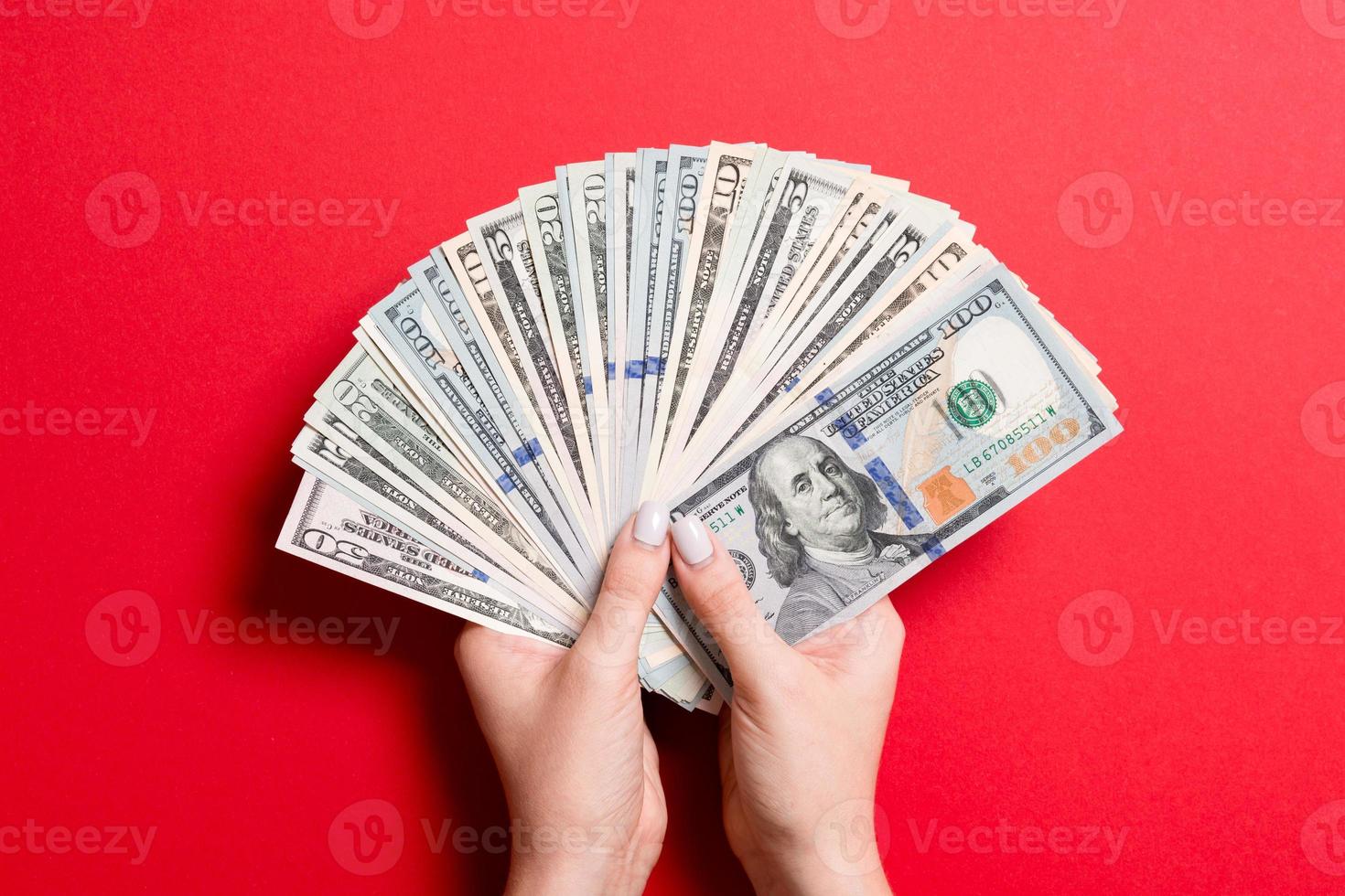 topp se av kvinna hand innehav en fläkt av pengar på färgrik bakgrund. olika dollar räkningar. kreditera och skuld begrepp foto