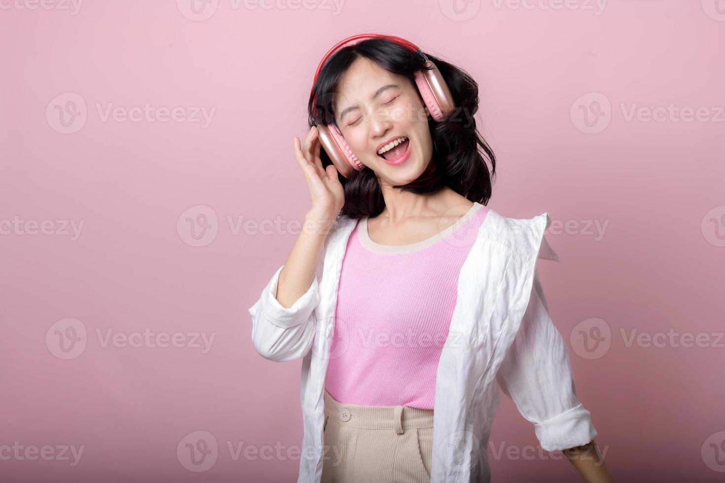 Lycklig ung asiatisk kvinna modell med eleganta trendig Sol glasögon njut av lyssnande musik förbi hörlurar audio och dans isolerat på rosa studio bakgrund. teknologi, flicka mode, tillbehör begrepp. foto