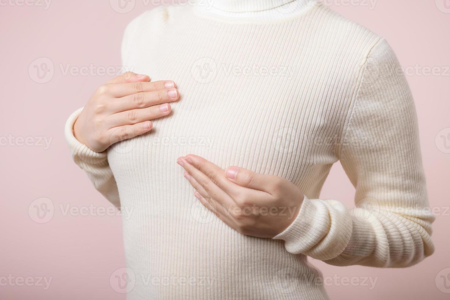 kvinna händer kontroll klumpar på henne bröst för tecken av bröst cancer på rosa bakgrund. sjukvård värld hälsa dag begrepp. foto