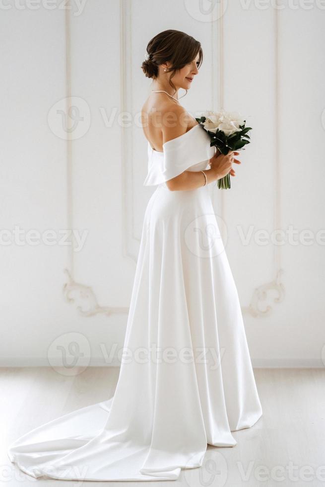 brunett brud i en tajt bröllop klänning i en ljus studio foto